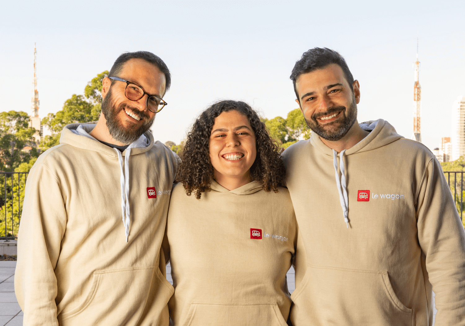 Three corporate professionals smiling and standing together outdoors.