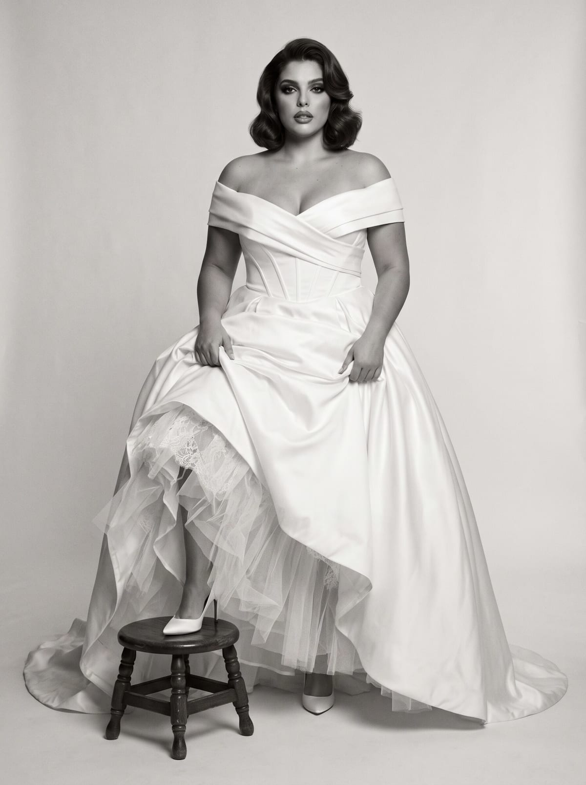 Black and white study of a satin ball gown with tulle petticoat over a wooden stool