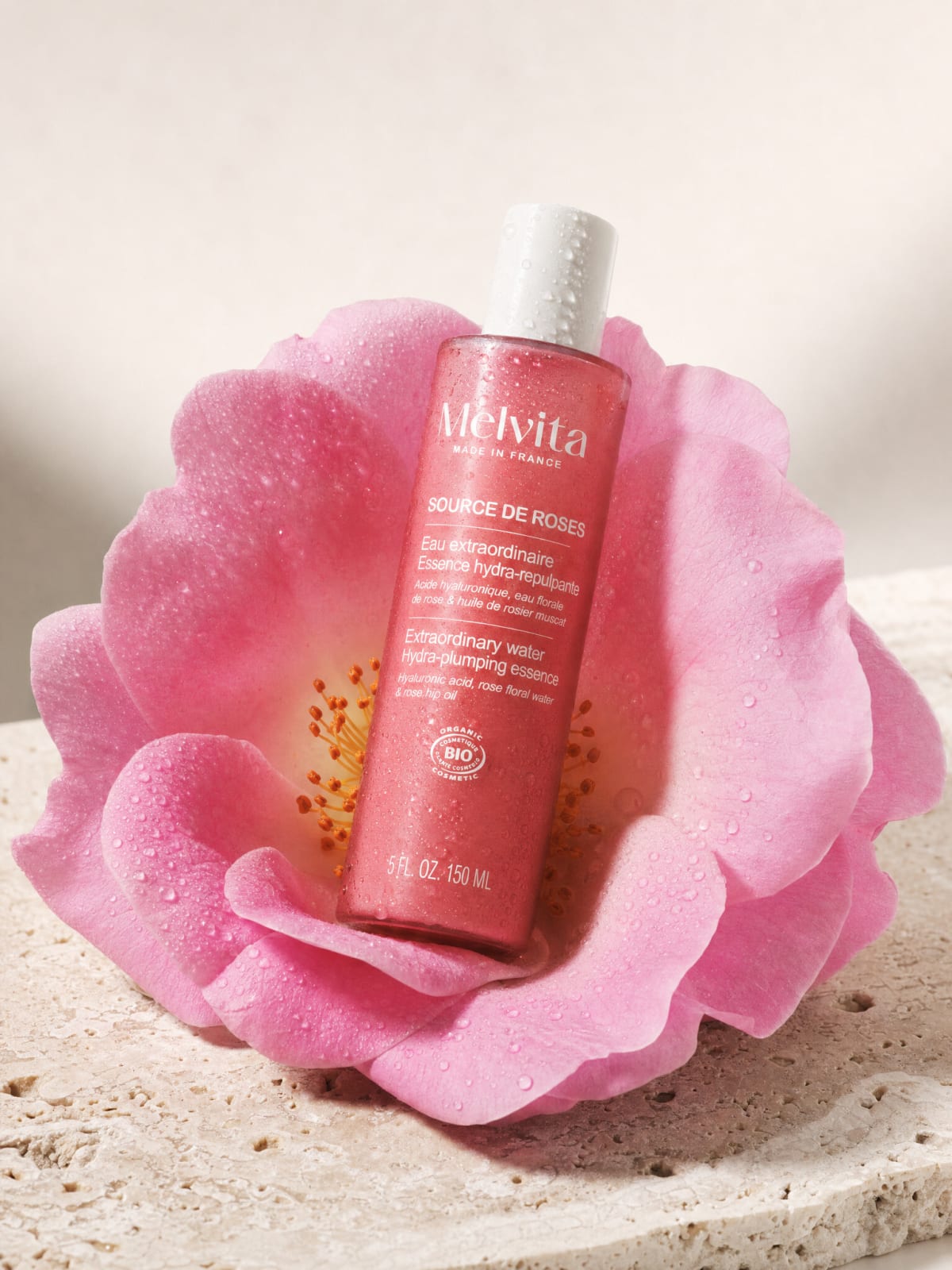 Melvita Source de Roses 瓶子躺在洞石上的一朵大粉花里