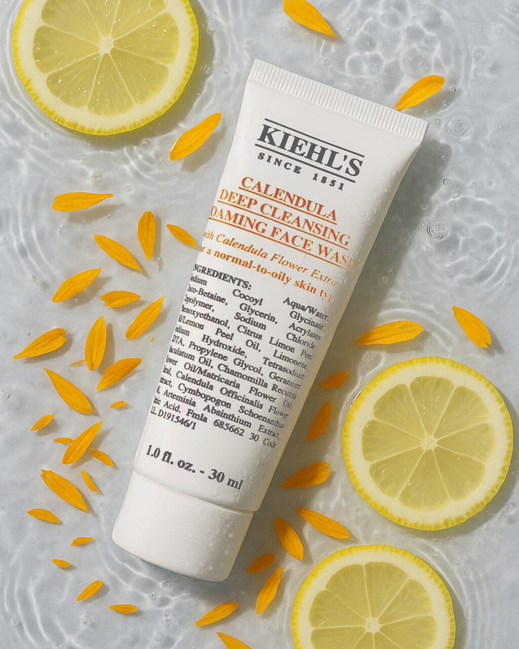 Kiehl's Calendula foaming face wash tube in water with lemon slices and marigold petals