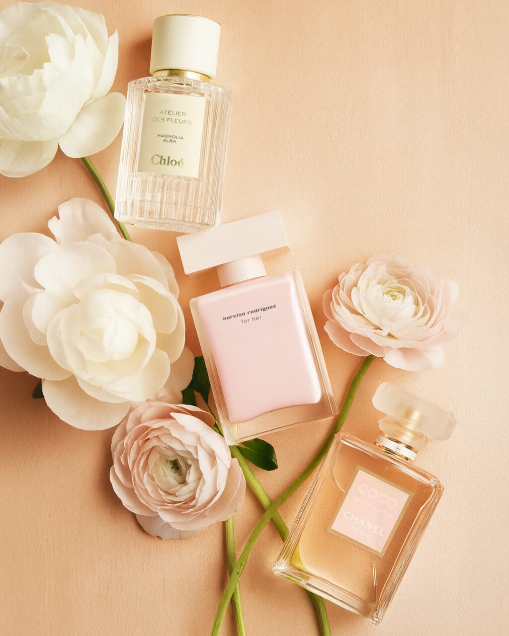 Chloé and Narciso Rodriguez perfume bottles among white peonies on peach