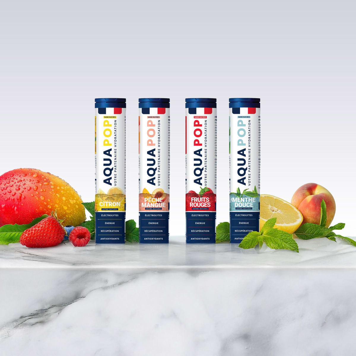 Four Aquapop tubes lined up on white marble with mango, berries, lemon and peach