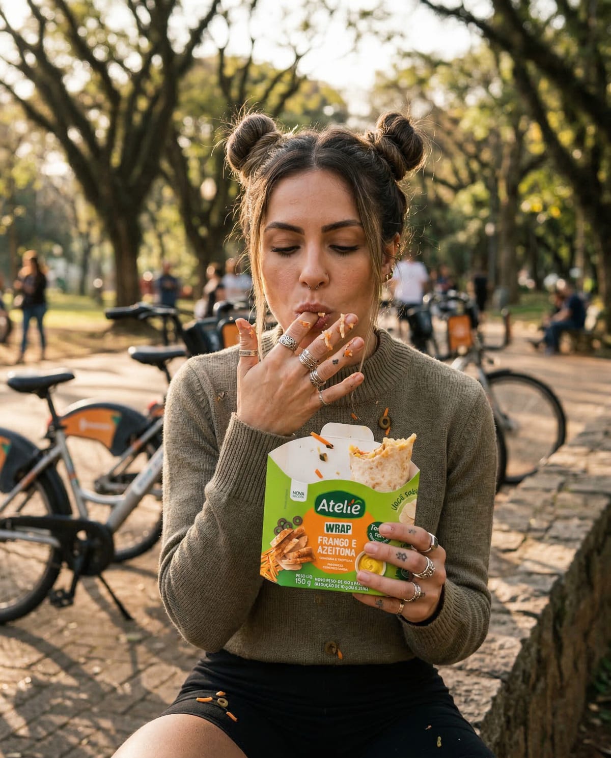 Woman in a brown sweater eating from an Ateliê wrap box near parked bicycles