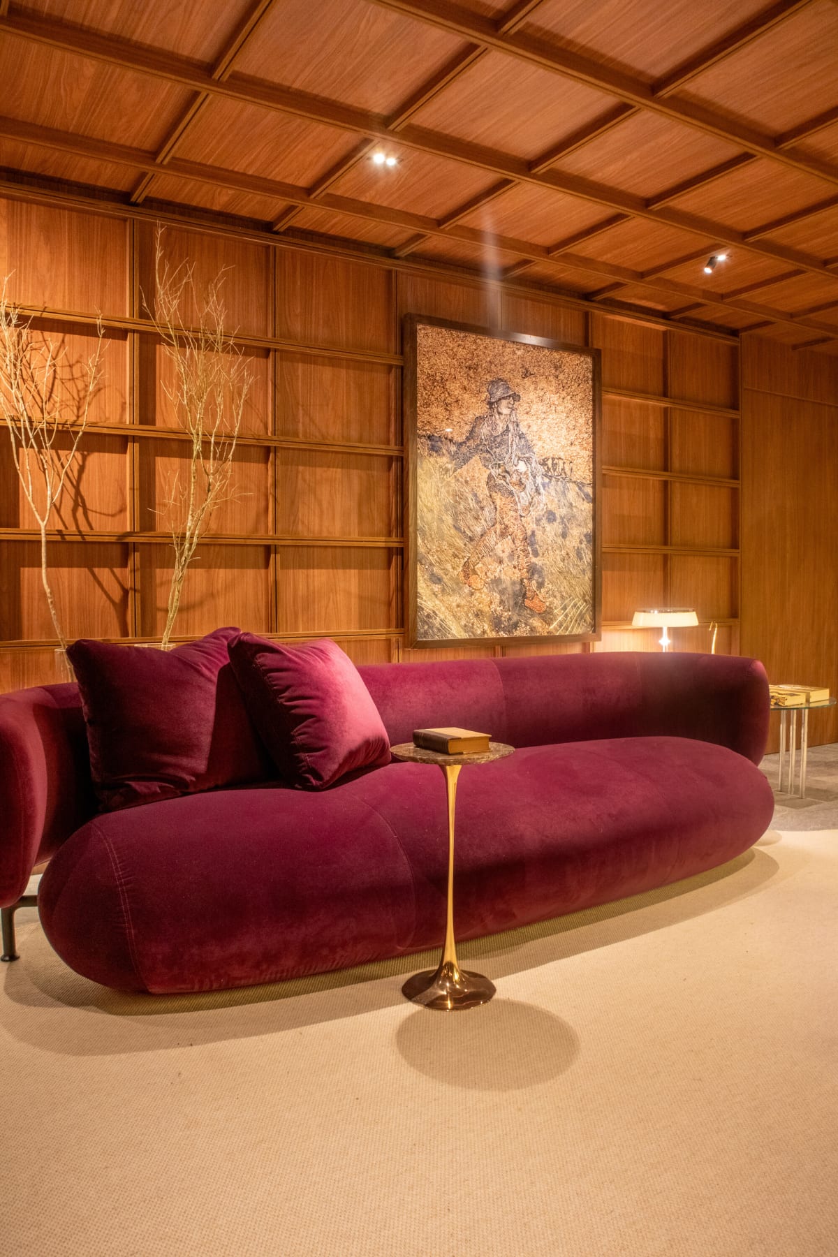 Plum velvet sofa and brass side table under a framed painting in a walnut grid room