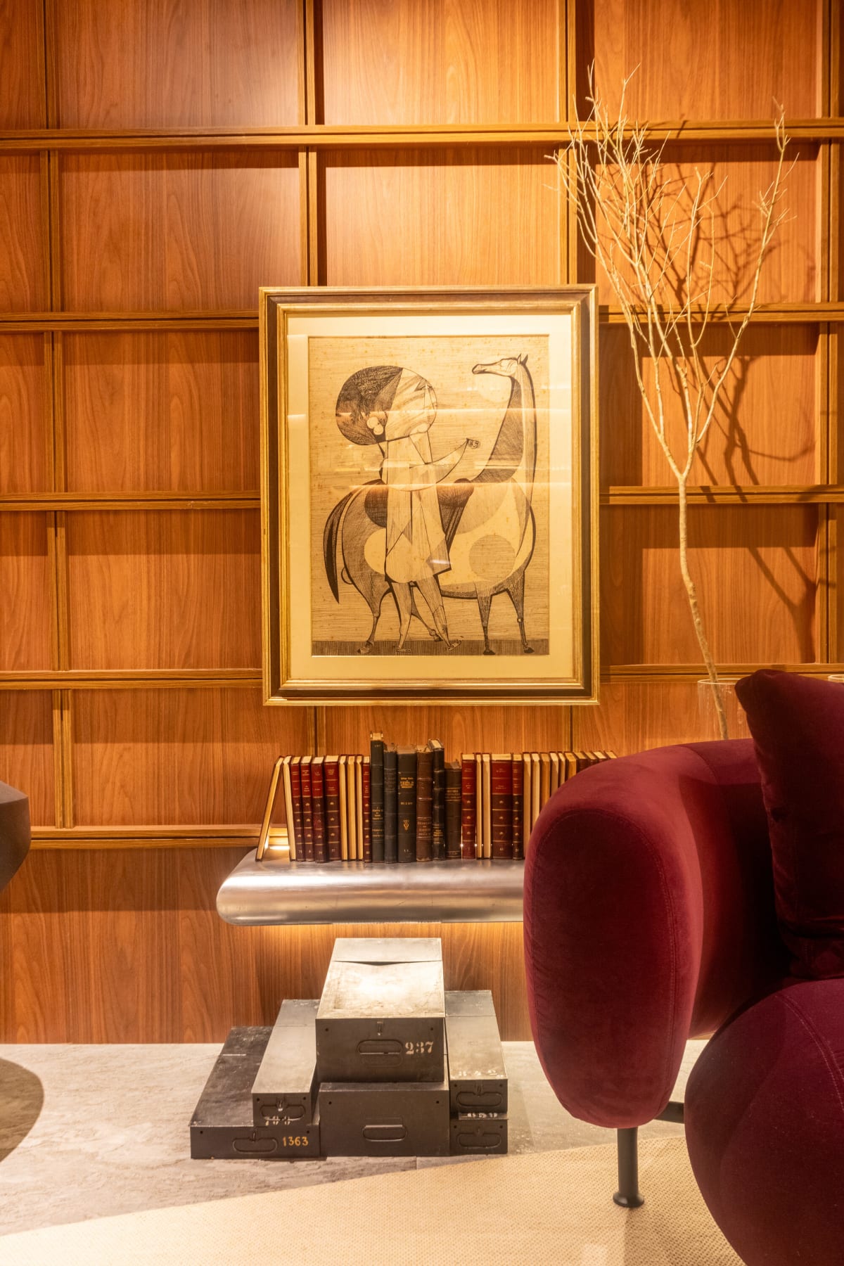 Framed horse drawing above stacked books and a plum velvet armchair