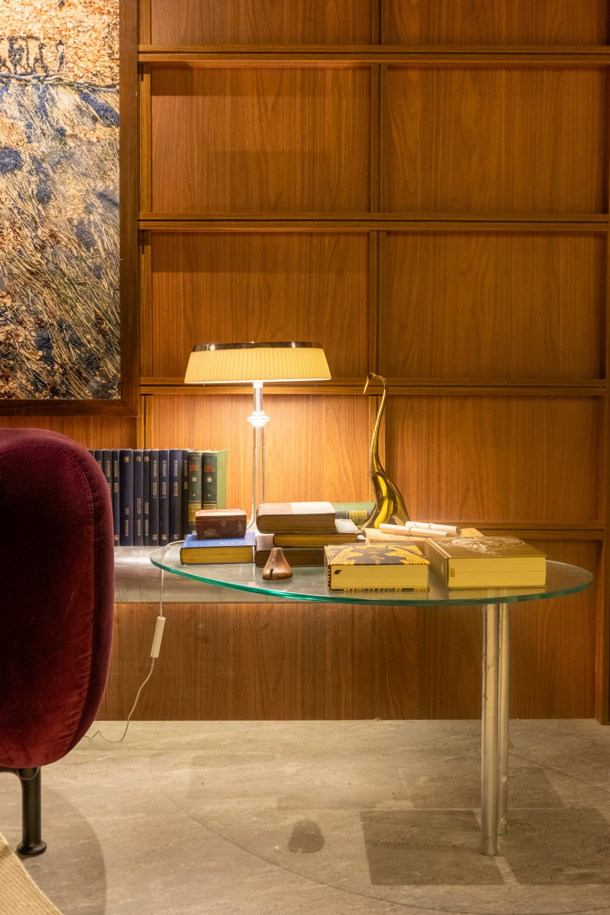 Glass top desk with a brass lamp, books and a plum velvet chair in walnut panelling