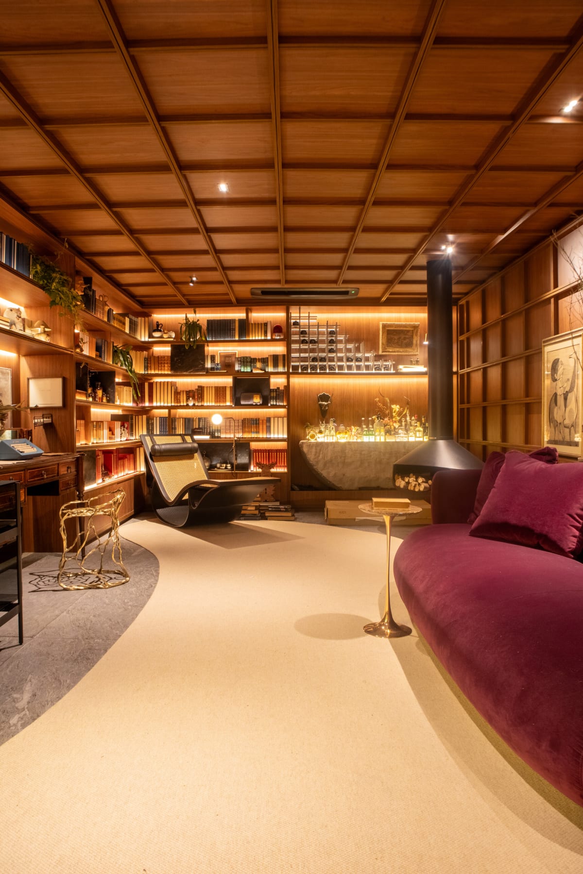 Reading room at CASACOR São Paulo with walnut grid ceiling, hanging fireplace and plum sofa