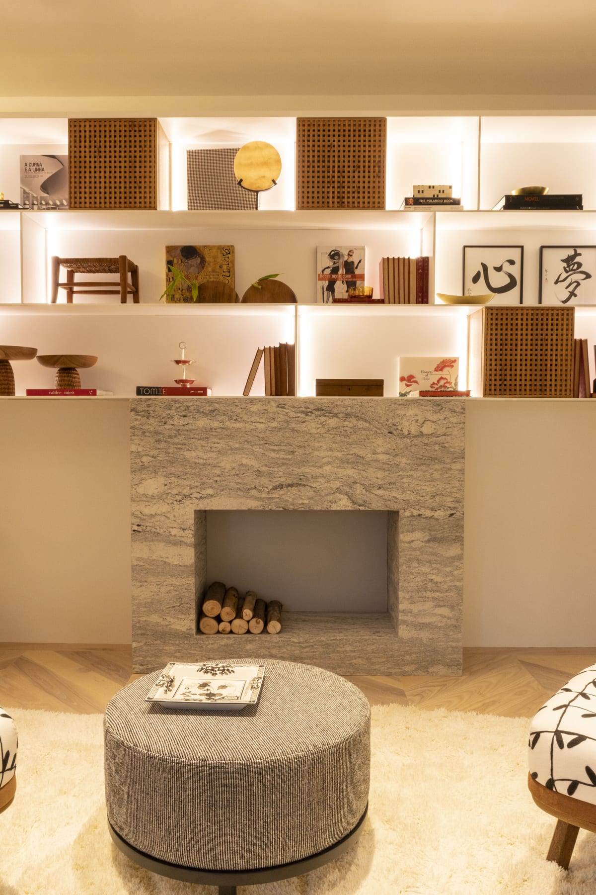 Marble fireplace with stacked logs under lit shelves of objects and calligraphy