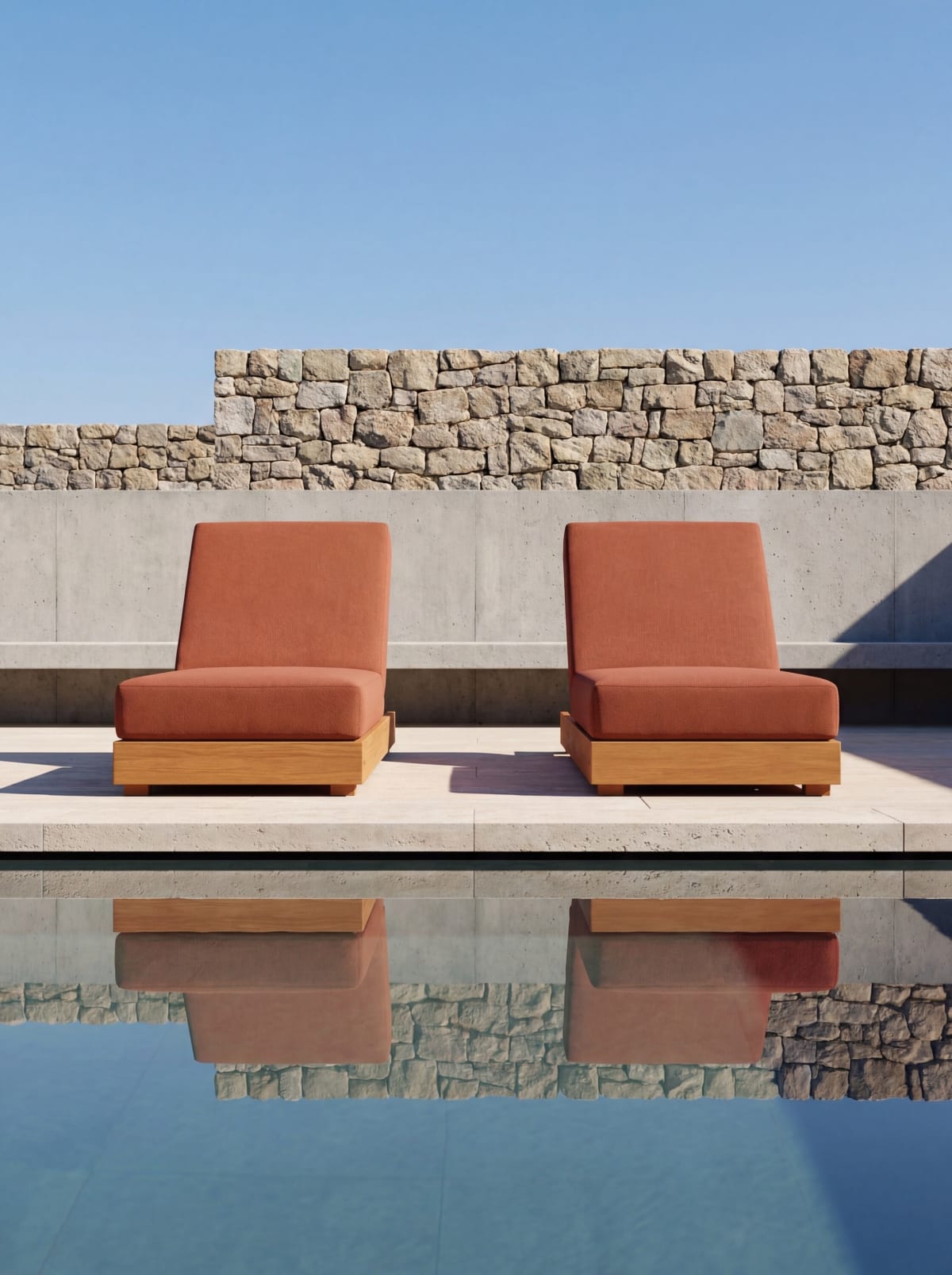 Two rust cushioned loungers reflected in a still pool before a stone wall