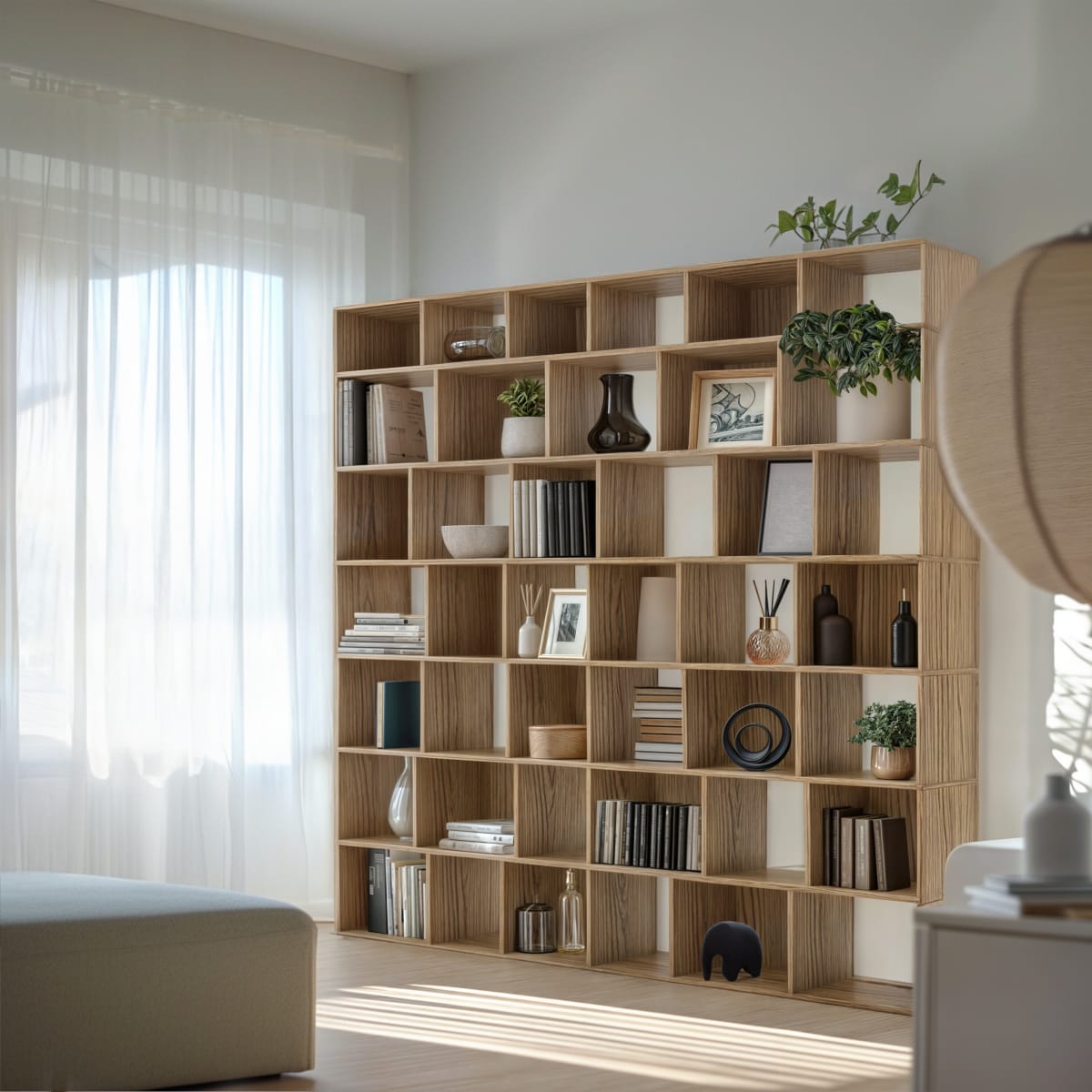 A tall oak Movêu bookcase filled with books, vases and plants beside sheer curtains