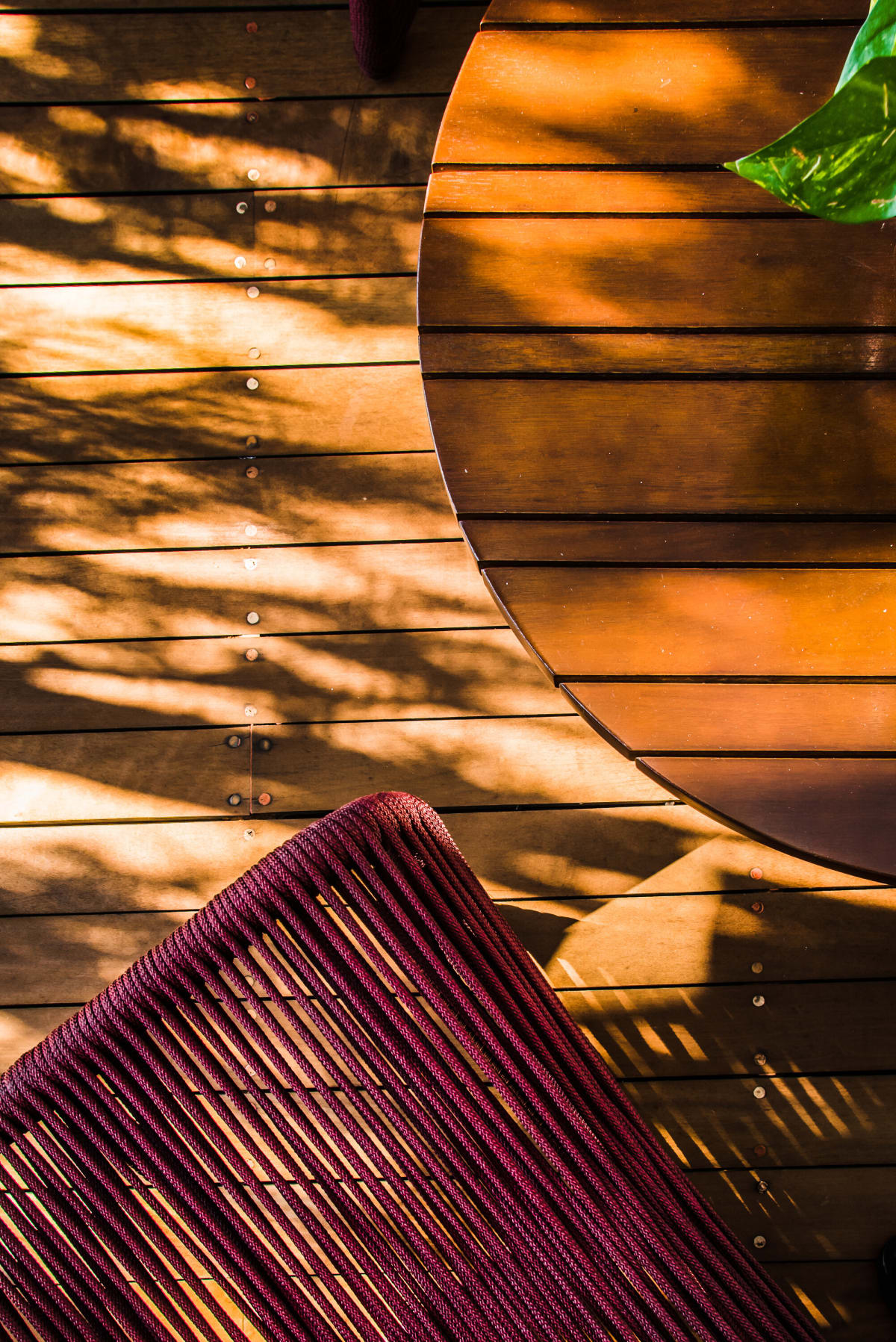 Close up of a burgundy woven chair against timber slats in raking sun