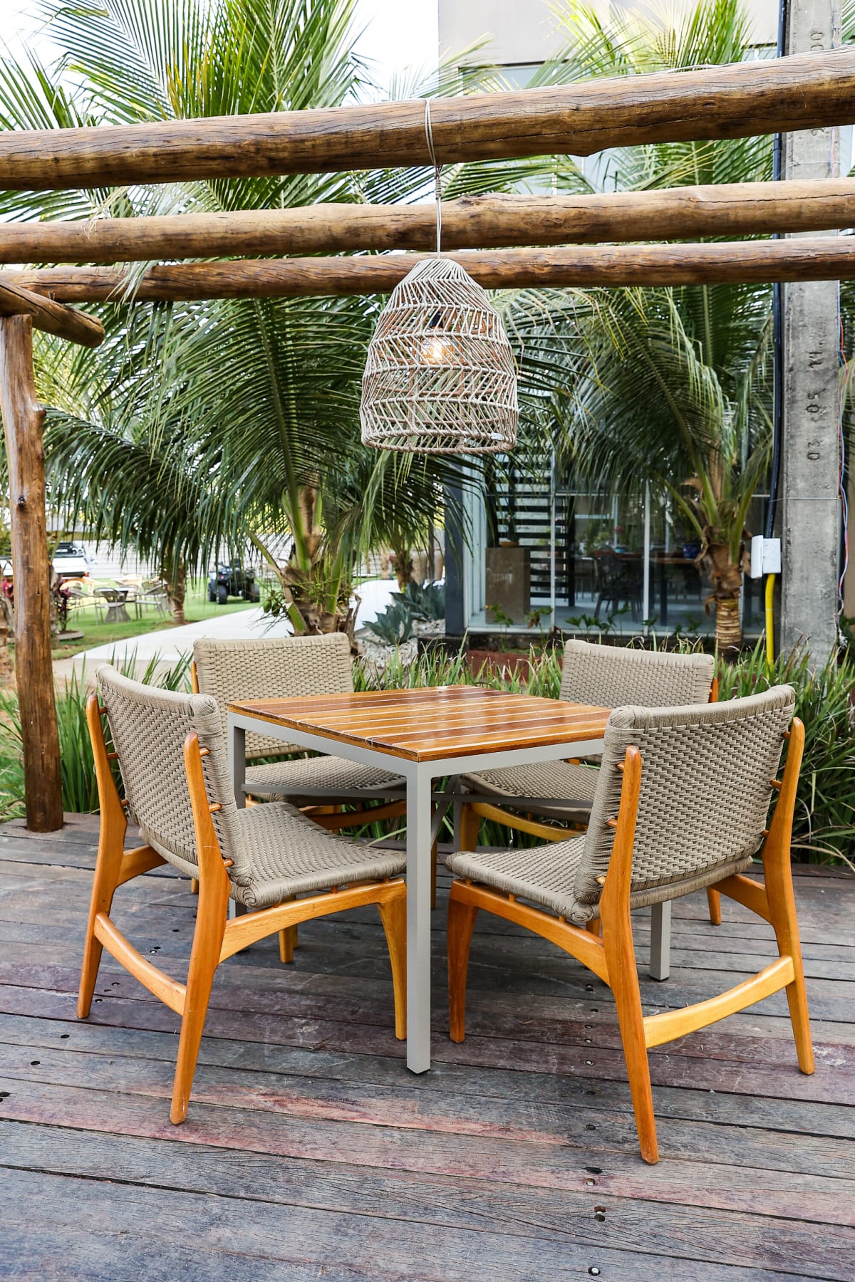 Teak dining table with rope chairs under a woven pendant and log beams
