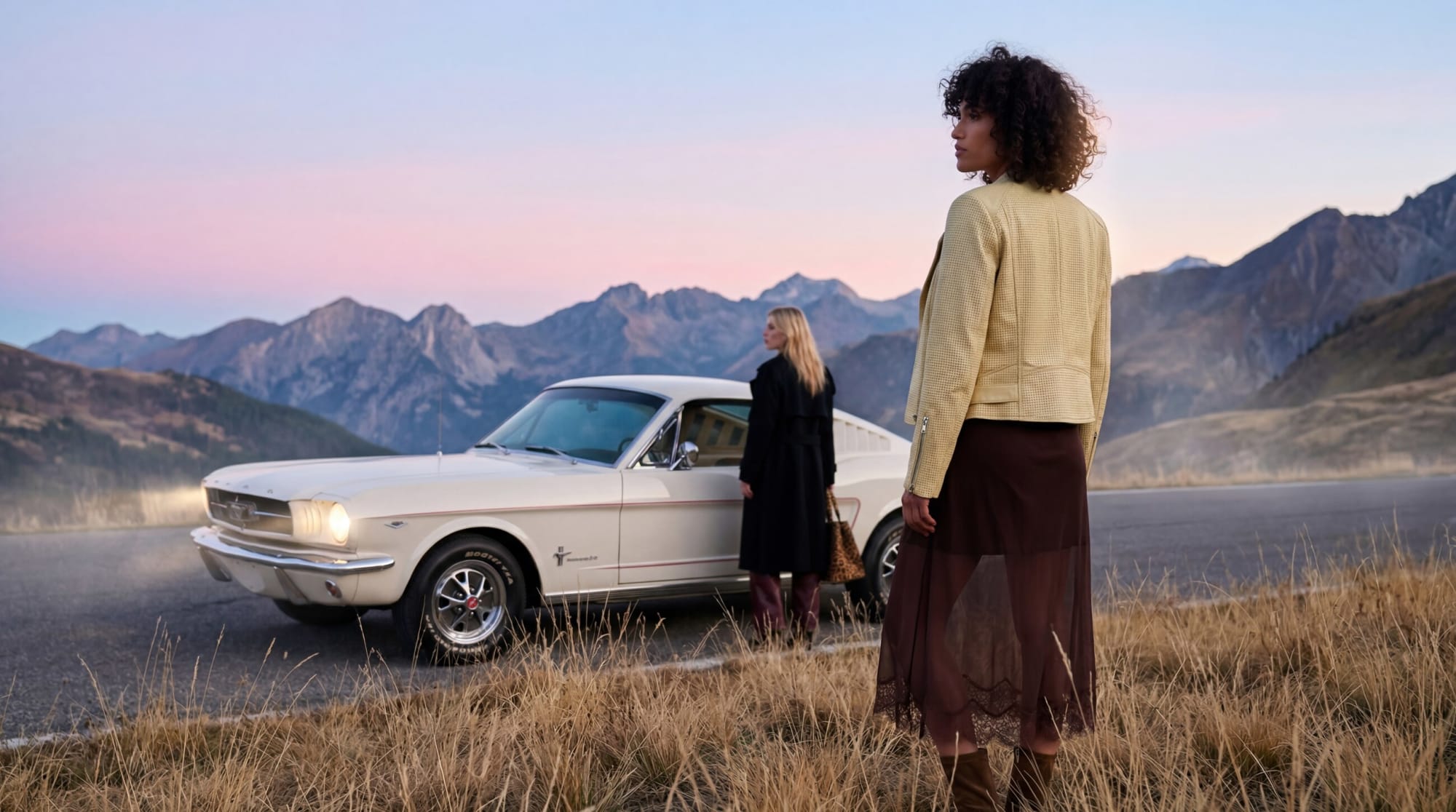 A yellow leather jacket and lace midi skirt beside a white vintage Mustang on a mountain road