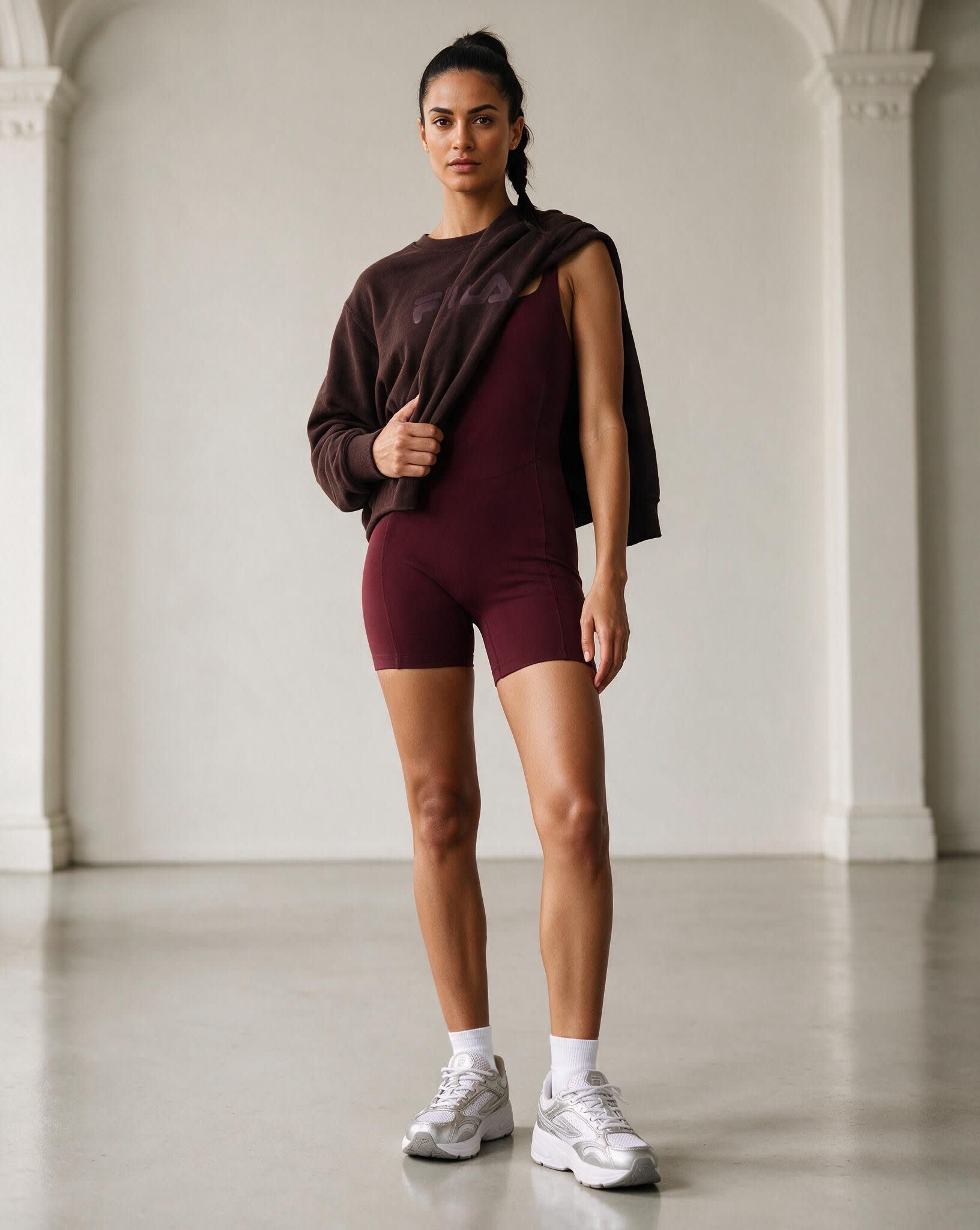 A model in burgundy bike shorts and a sweatshirt over one shoulder in a white loft studio