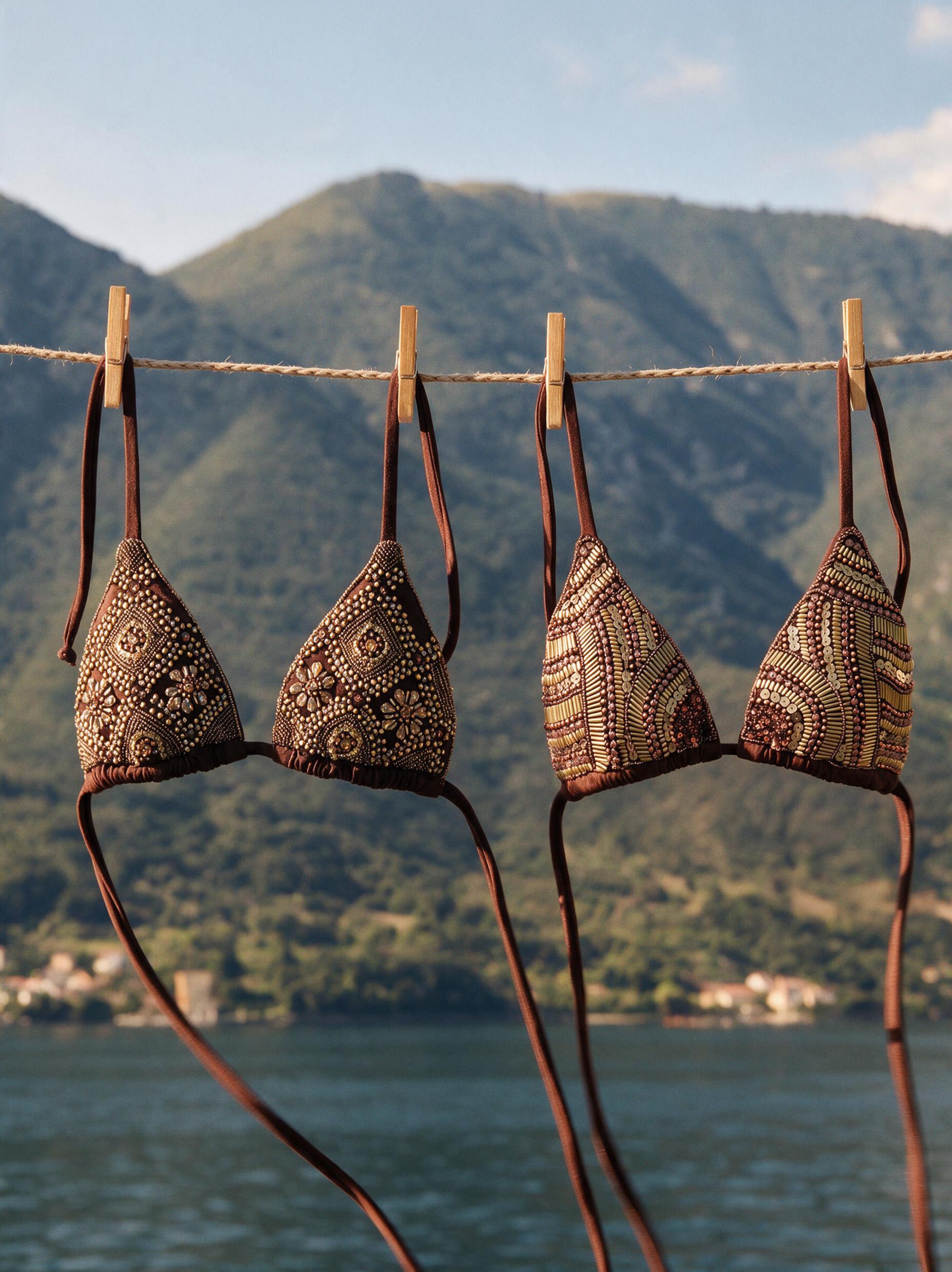 Four beaded Palermo bikini tops pegged on a clothesline above a bay with green mountains