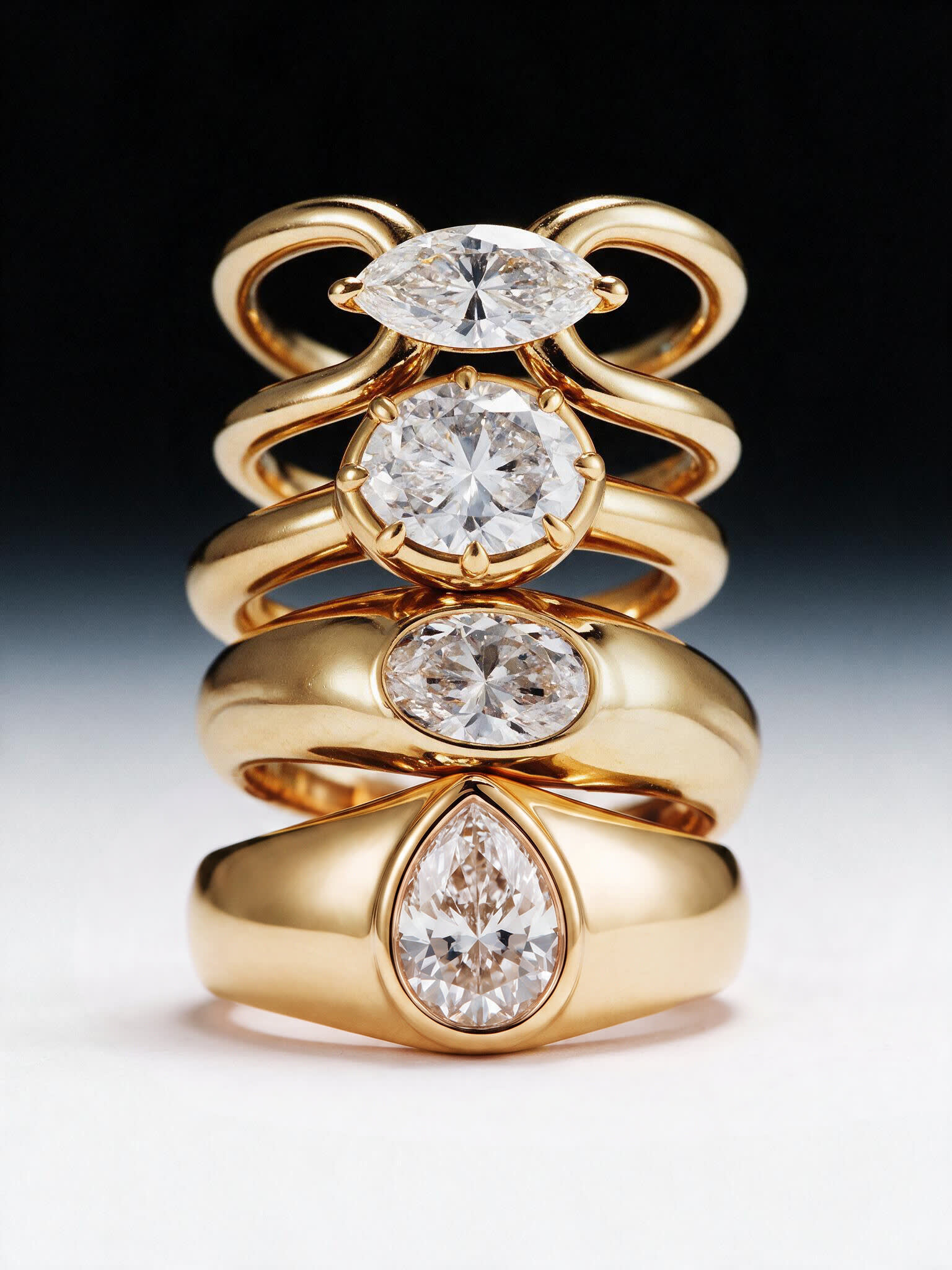 Four stacked gold rings set with marquise, oval and pear cut diamonds on a black gradient
