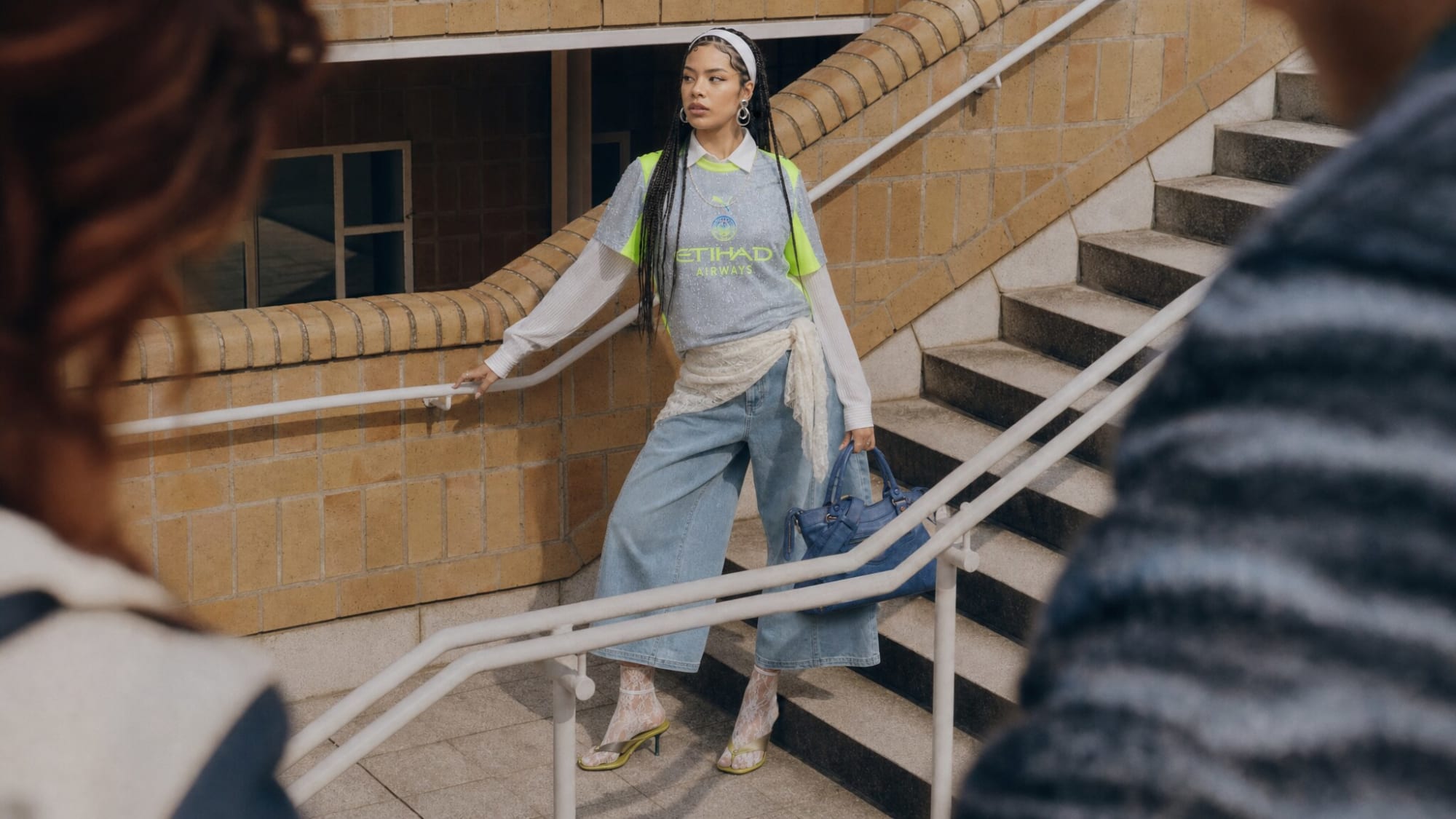 Modelo de camisa de futebol azul-clara e jeans largo descendo uma escadaria