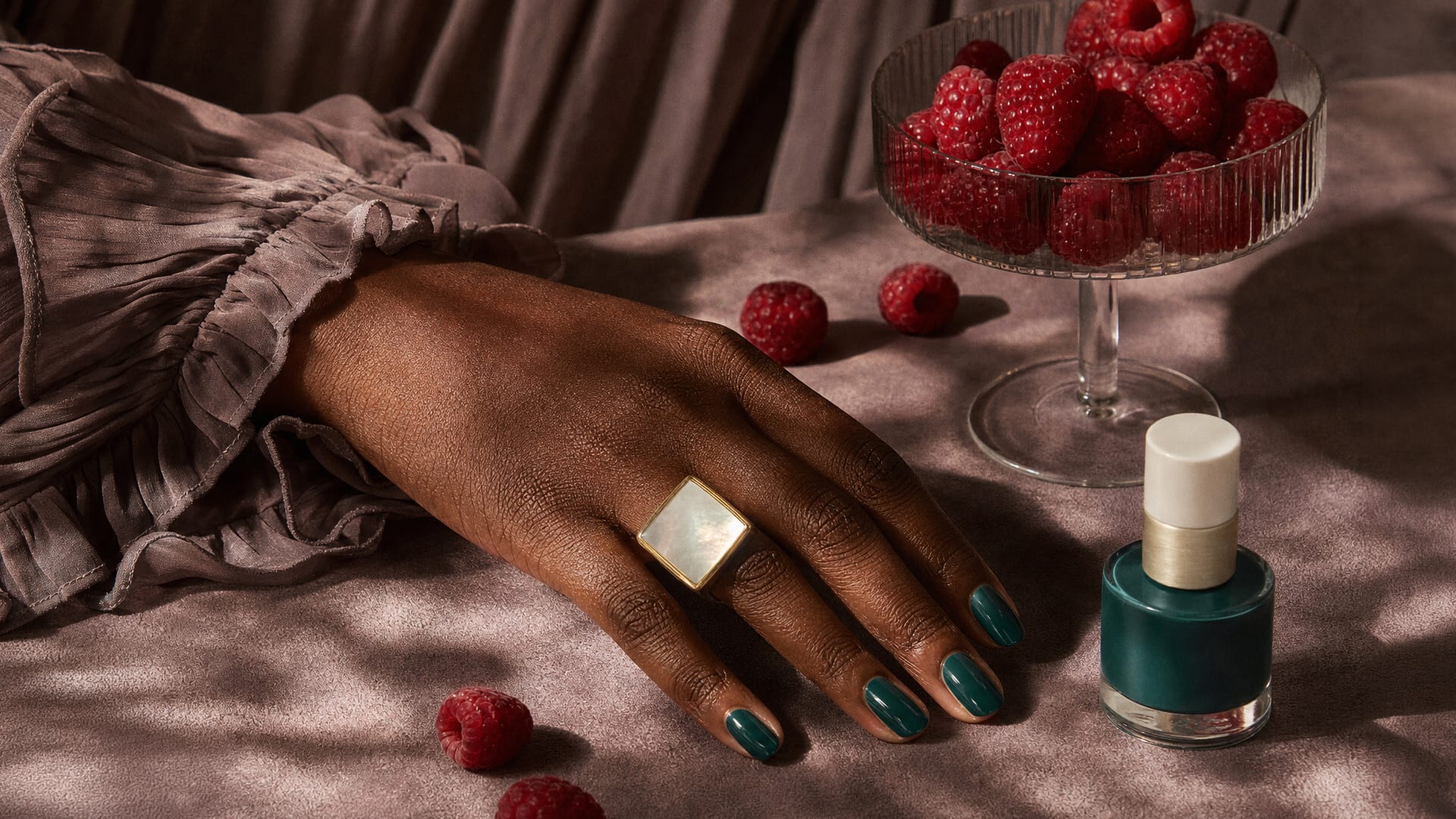 Hand with green nail polish and a gold ring beside a polish bottle and raspberries