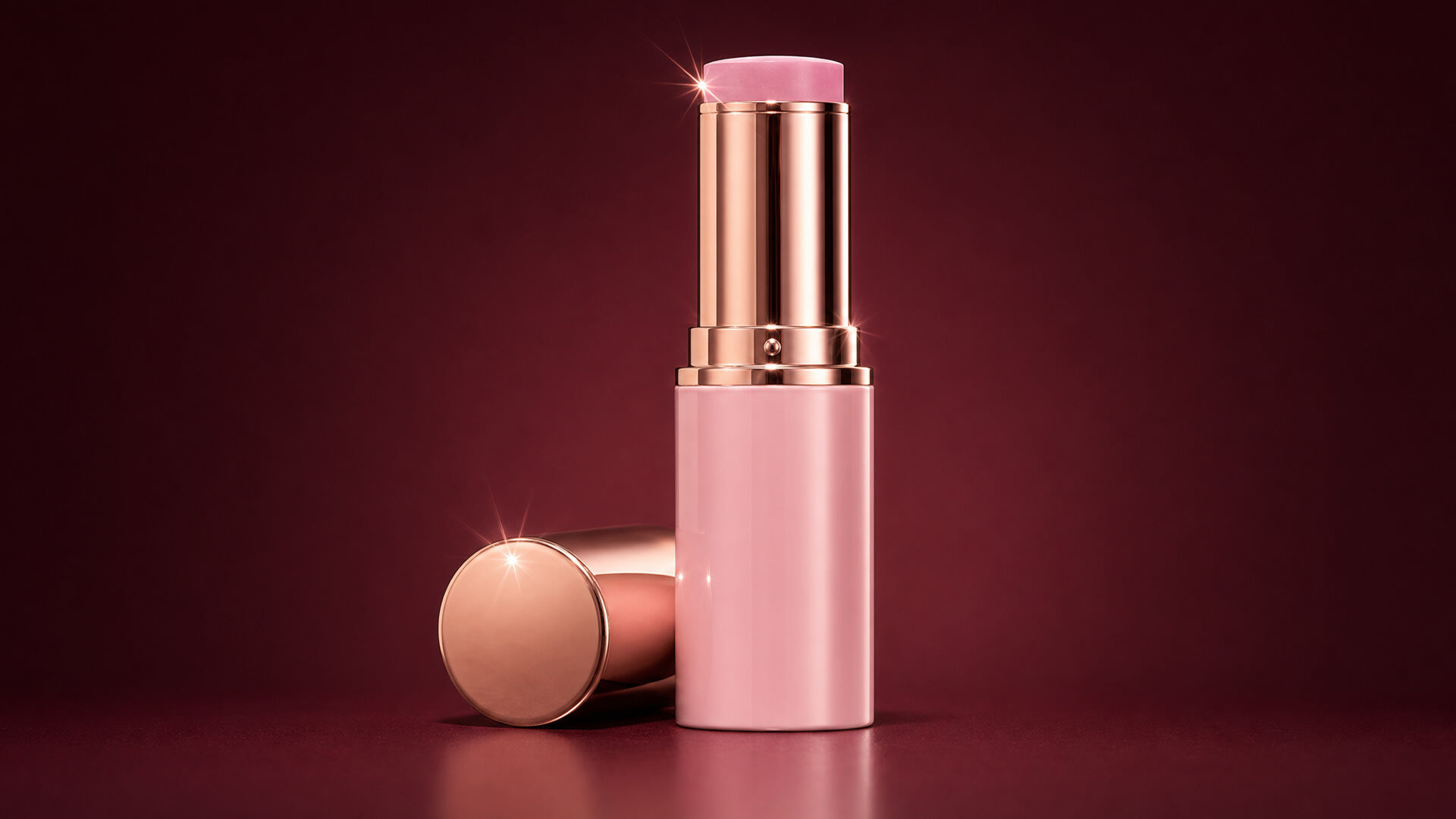 Pink lipstick in a rose gold case standing on a glossy deep red studio set