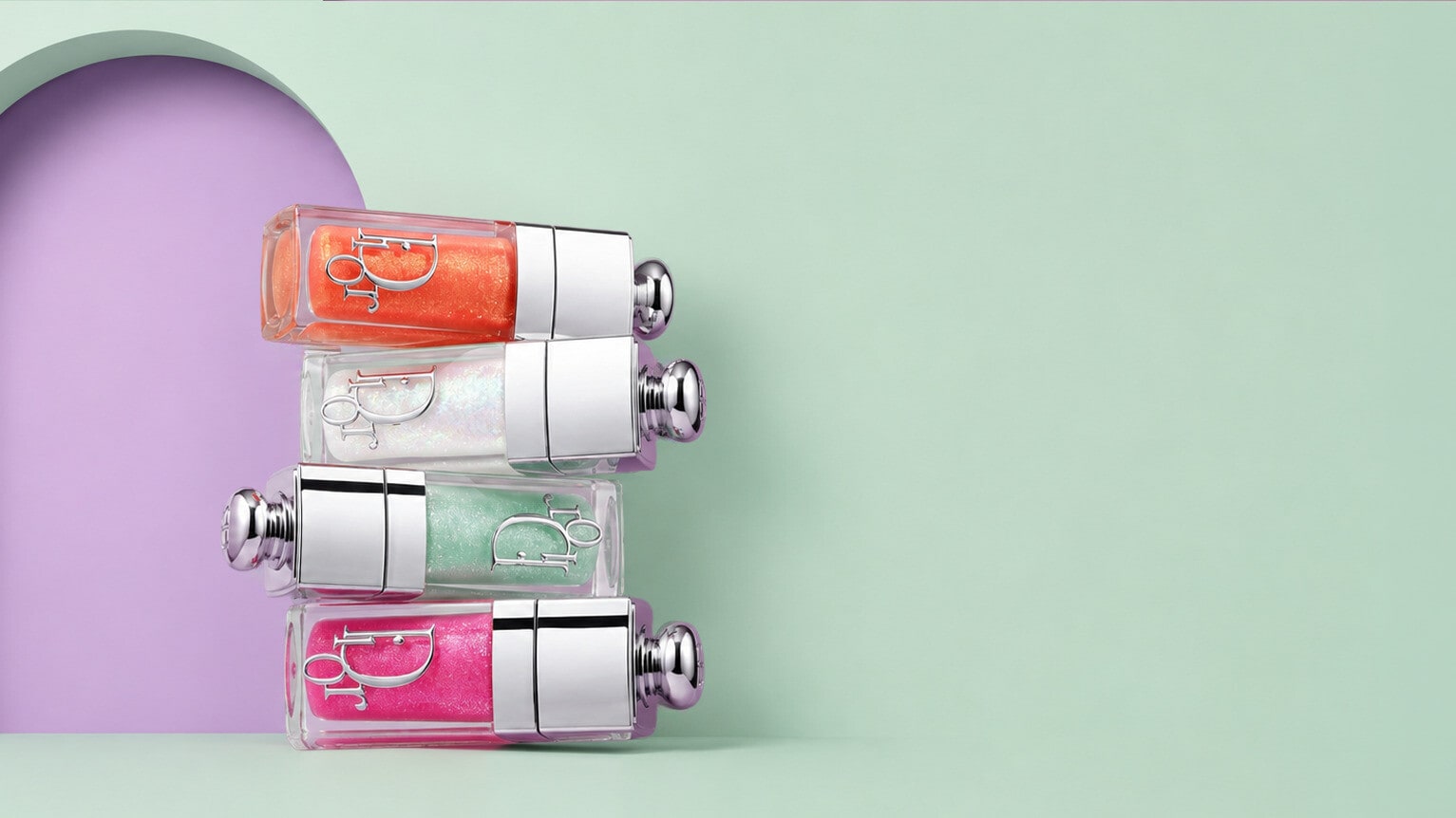 Four lip oil bottles stacked on their sides against a lilac arch on mint green