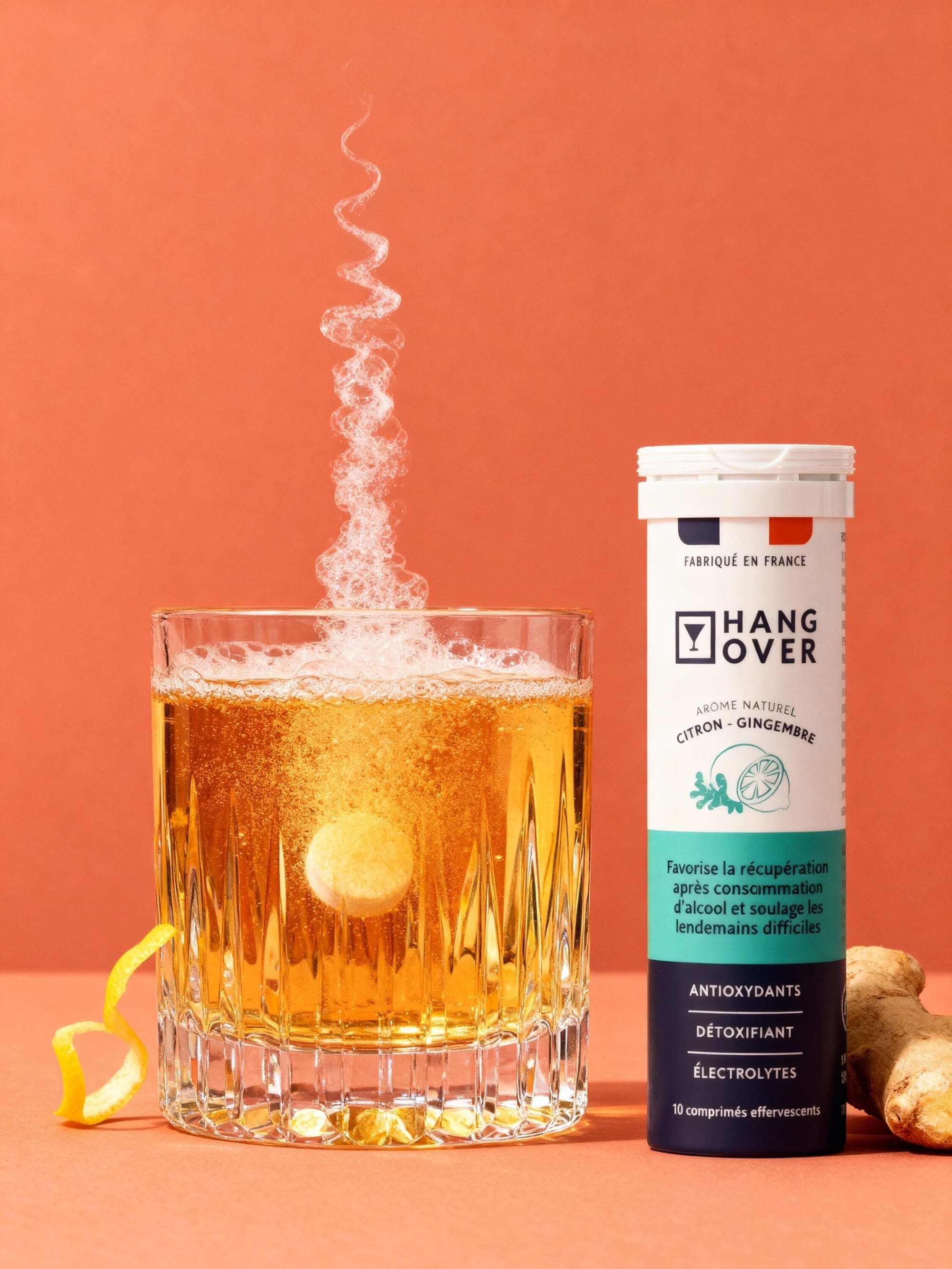 Effervescent tablet fizzing in a glass beside a Hangover lemon ginger tube on coral