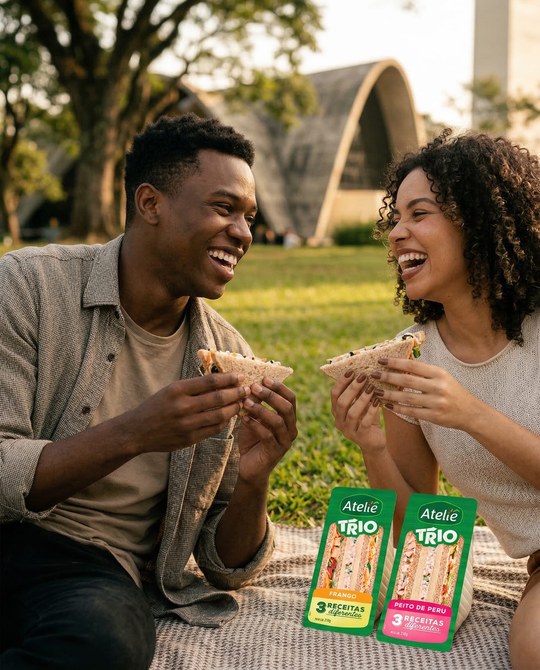 Couple on a picnic blanket in a park eating sandwiches from Ateliê Trio packs