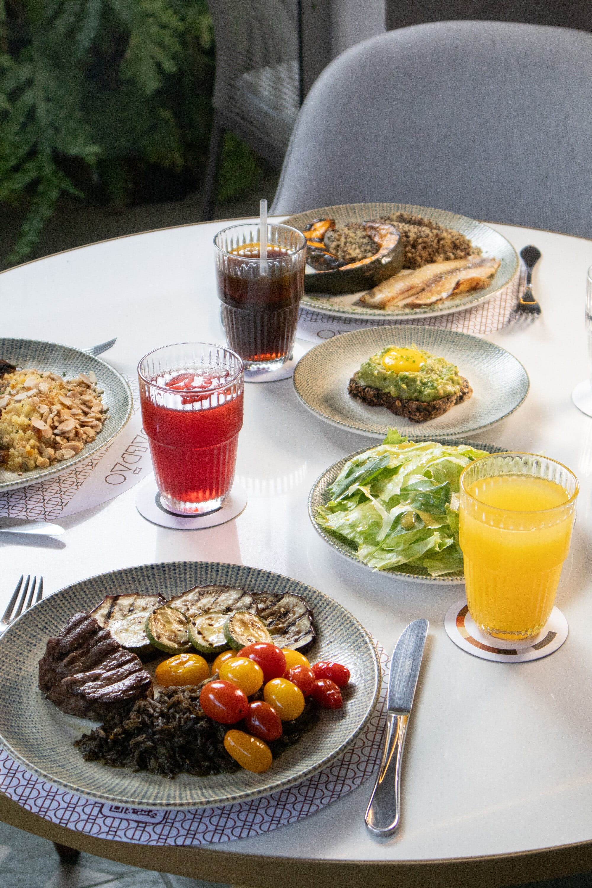 Restaurant table set with grilled vegetables, salads, juices and soda on white marble