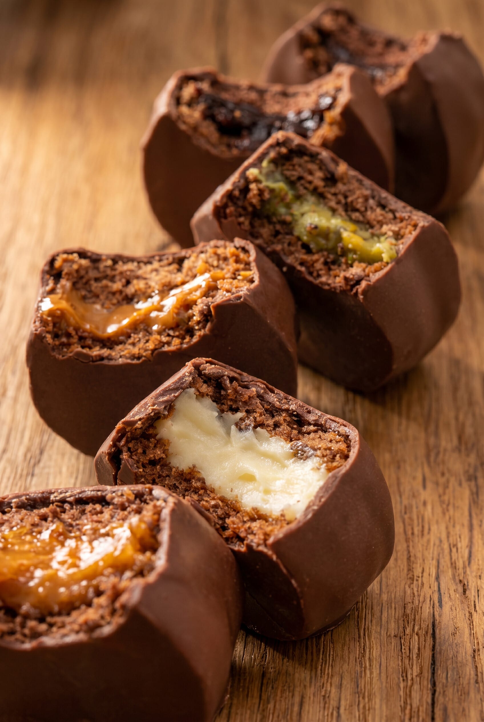 Close up of halved chocolate bonbons with caramel, pistachio and cream on dark wood