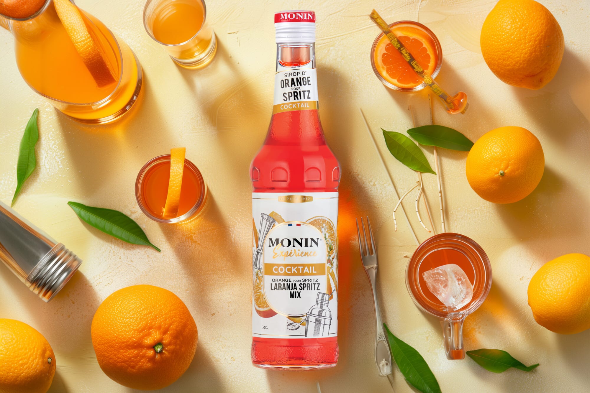 Monin Orange Spritz syrup bottle flat lay with oranges, spritz glasses and leaves on cream