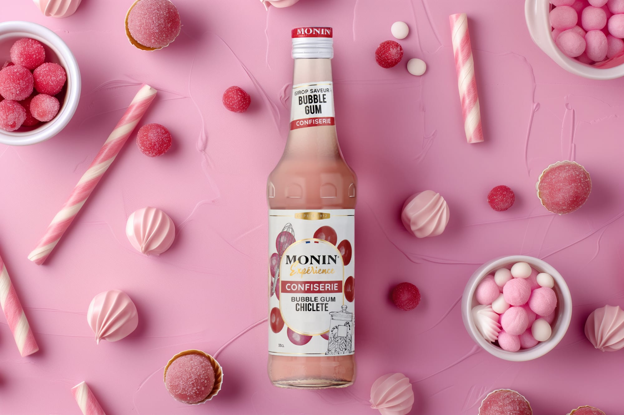 Monin bubble gum syrup bottle among pink candies, meringues and candy sticks