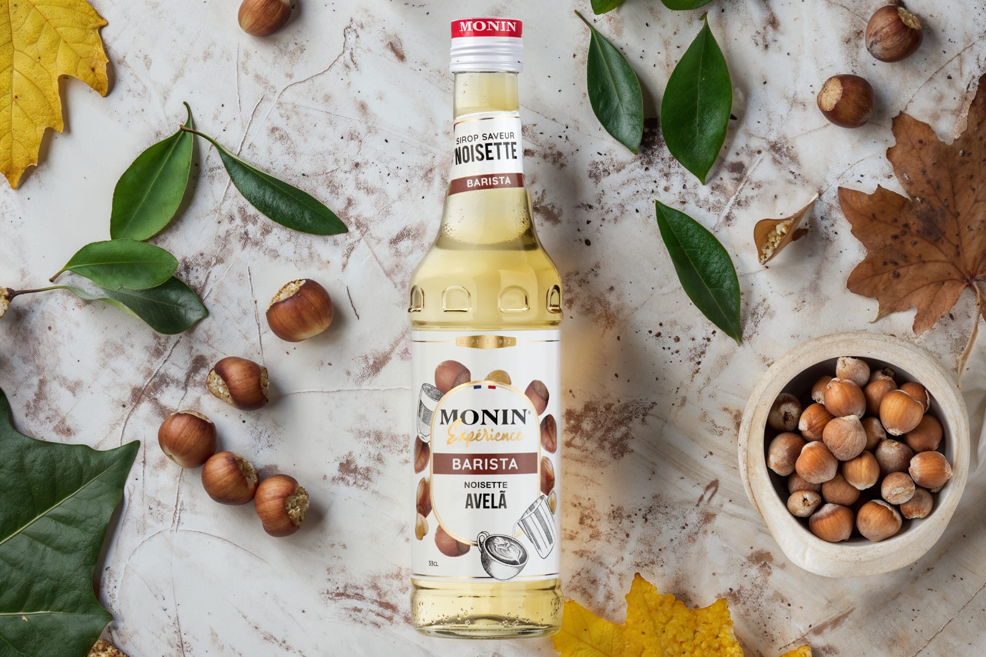 Monin hazelnut syrup bottle with hazelnuts and autumn leaves on white marble