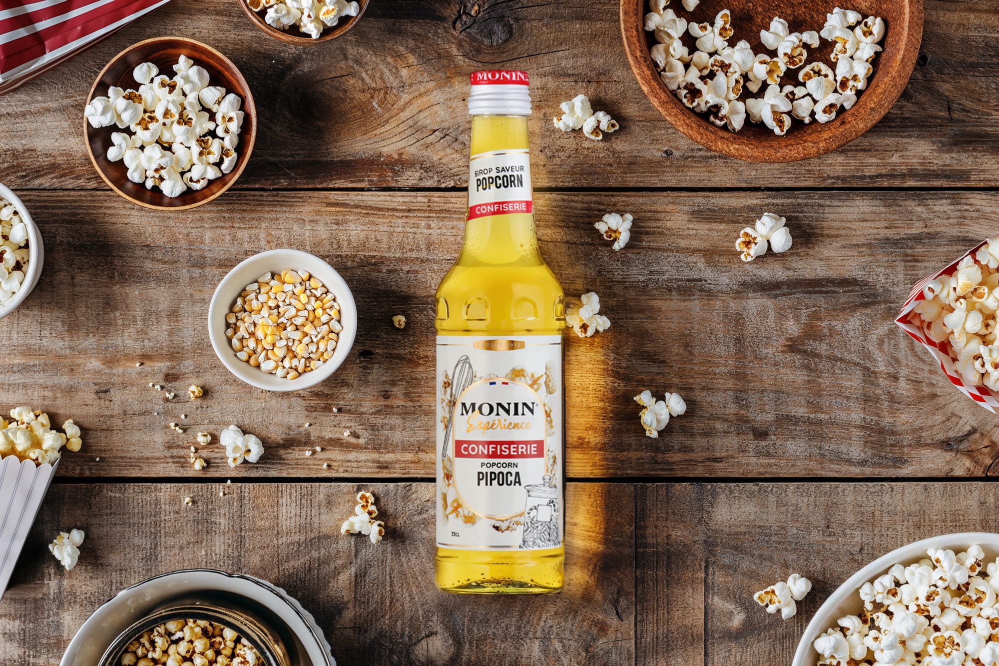 Monin popcorn syrup bottle with bowls of popcorn and kernels on a wooden table