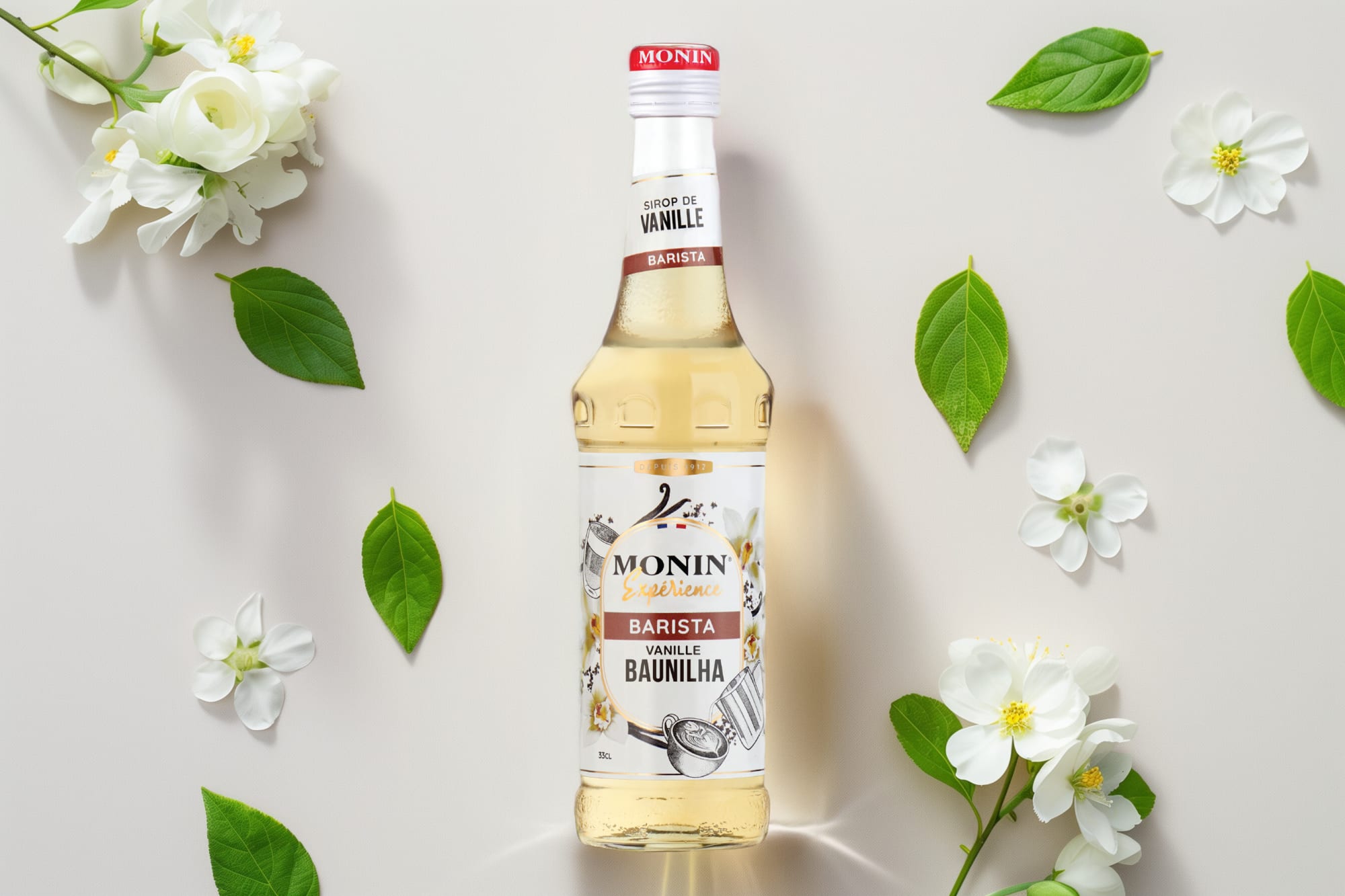 Monin vanilla syrup bottle with white flowers and green leaves on a pale grey surface