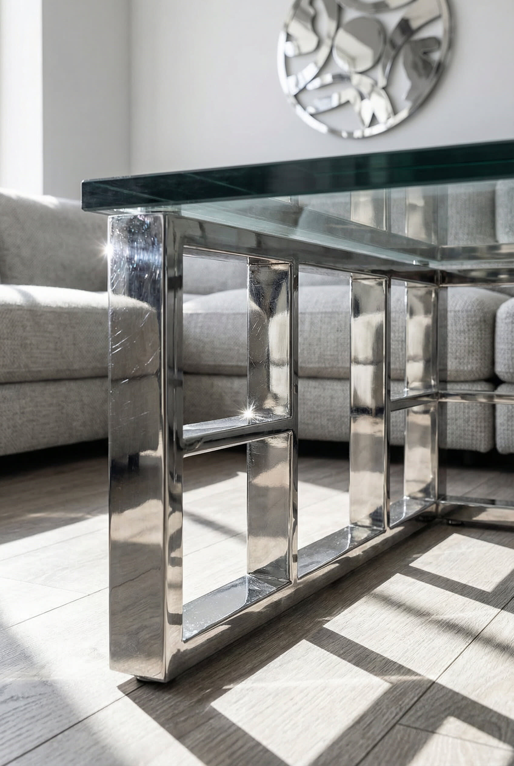 The mirrored steel frame of a glass coffee table in front of a grey sofa