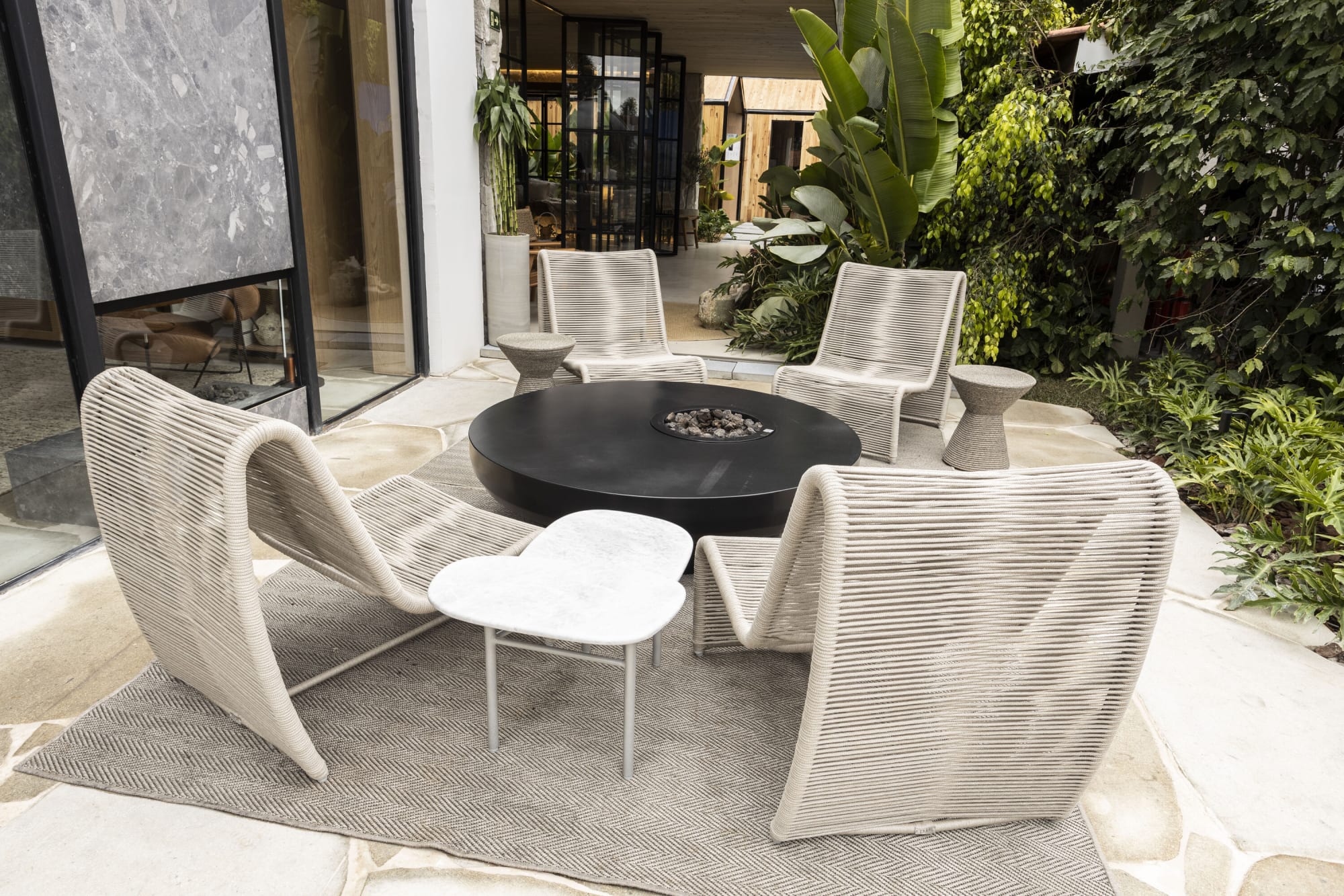 Sillones de cuerda blancos alrededor de una mesa redonda negra en un patio con jardín