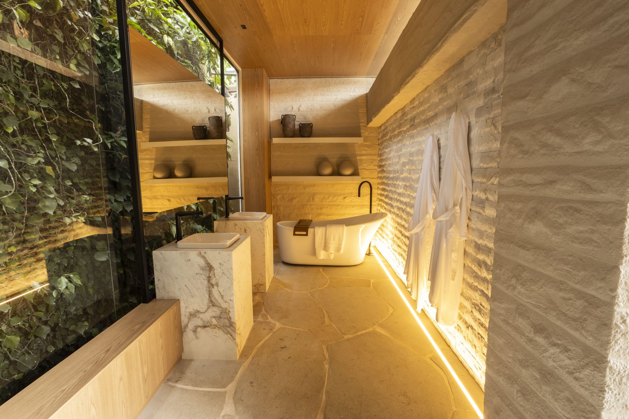 Baño de travertino en CASACOR Curitiba con lavabos de piedra, tina exenta y muro verde