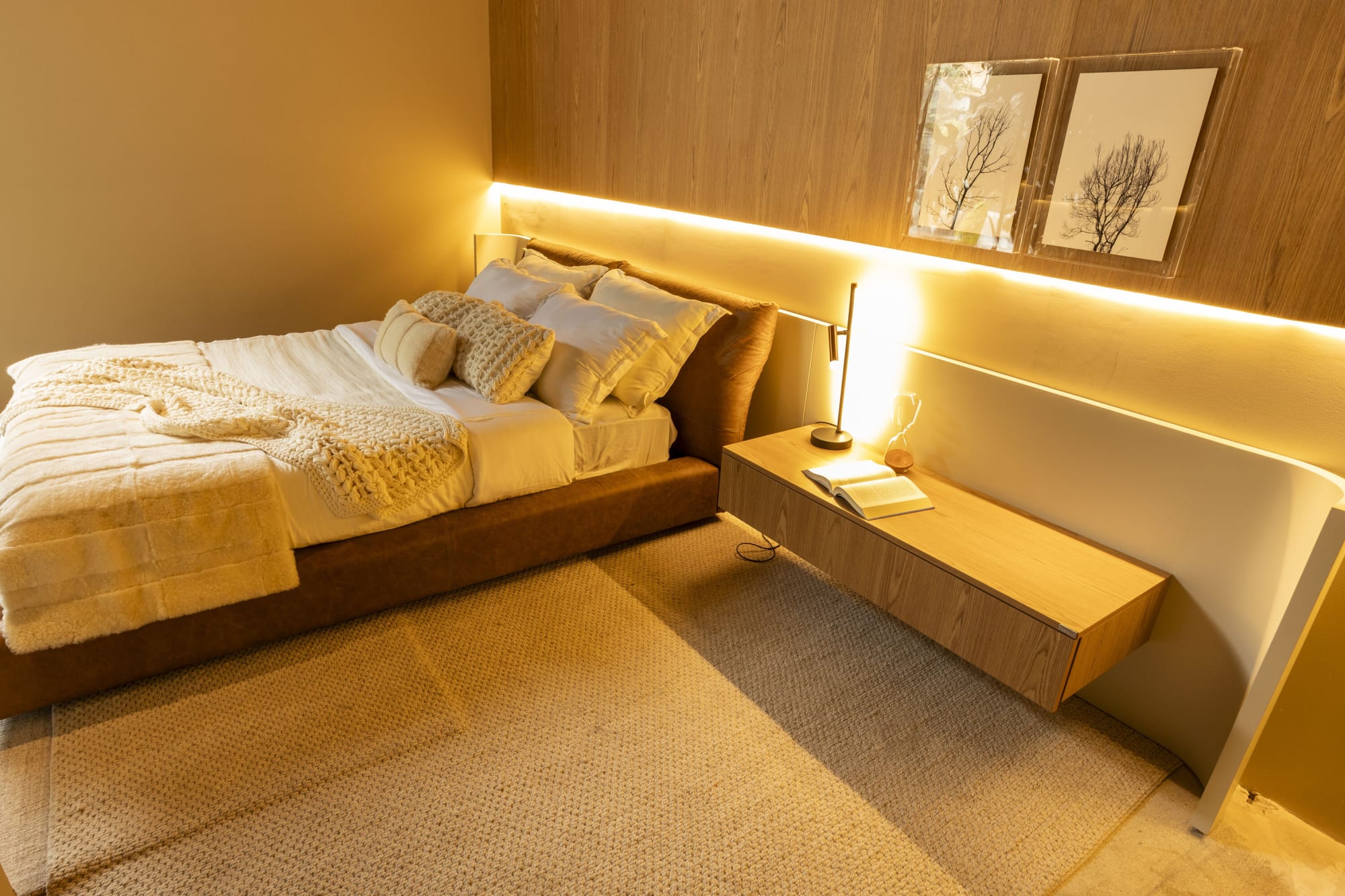 Recámara de roble con cama de lino blanco, repisa de cabecera iluminada y grabados de árboles enmarcados