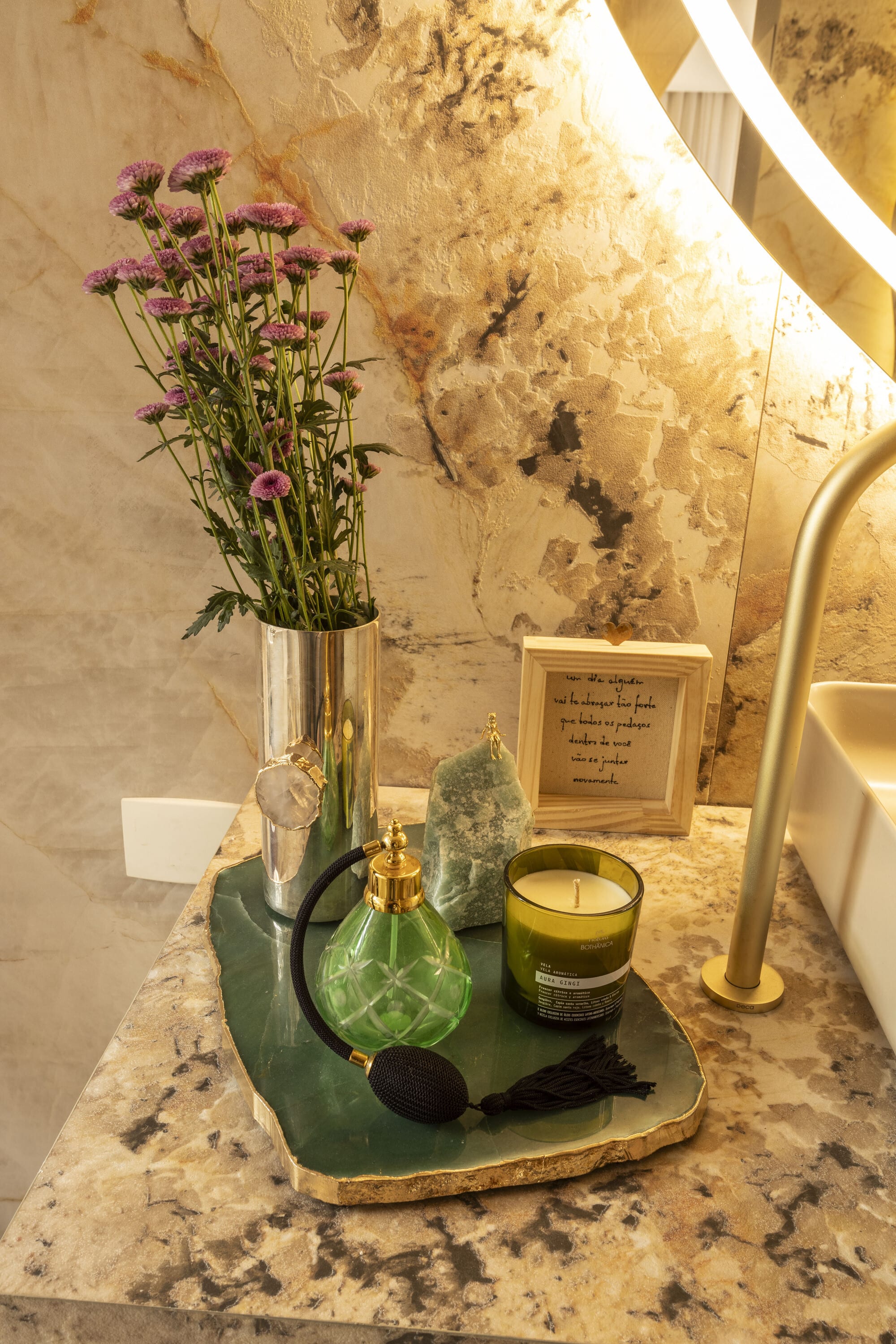 Green perfume bottle, candle and dried flowers on a stone tray beside a brass tap
