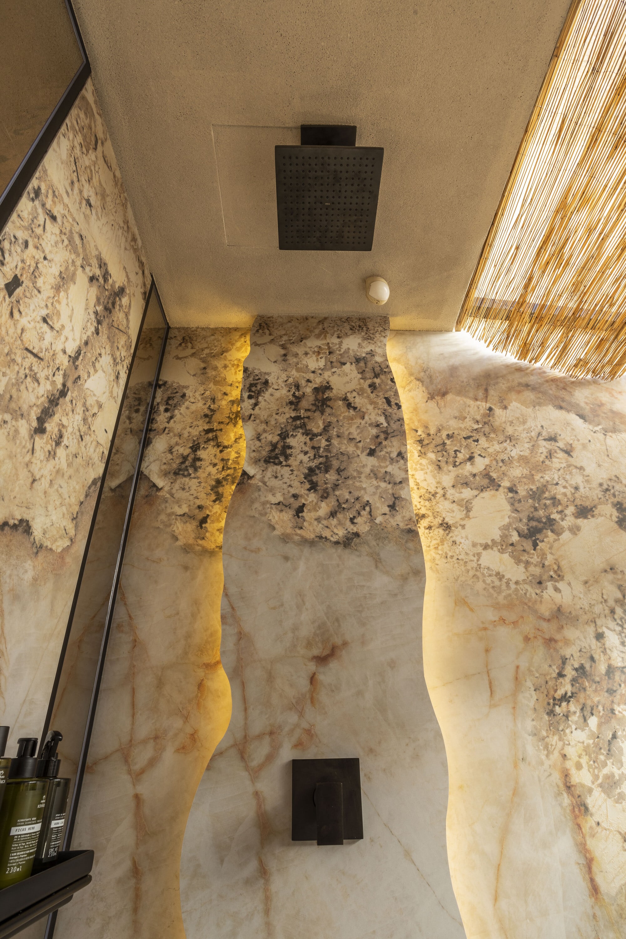 Shower lined with veined granite slabs and backlit edges under a black rain head