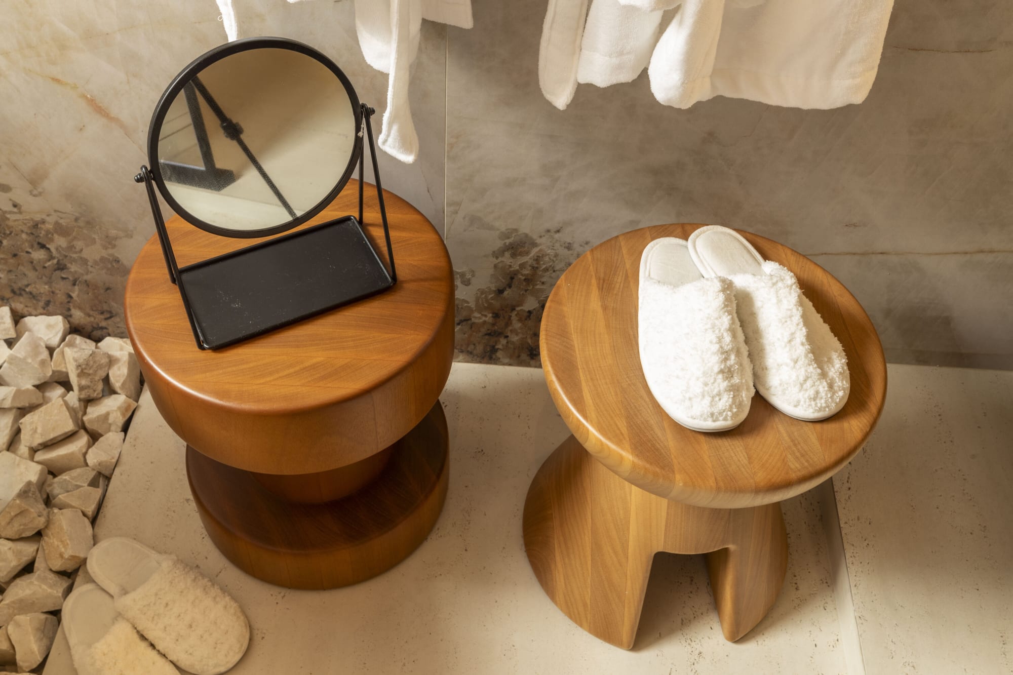 Two wooden stools holding a tabletop mirror and white towelling slippers