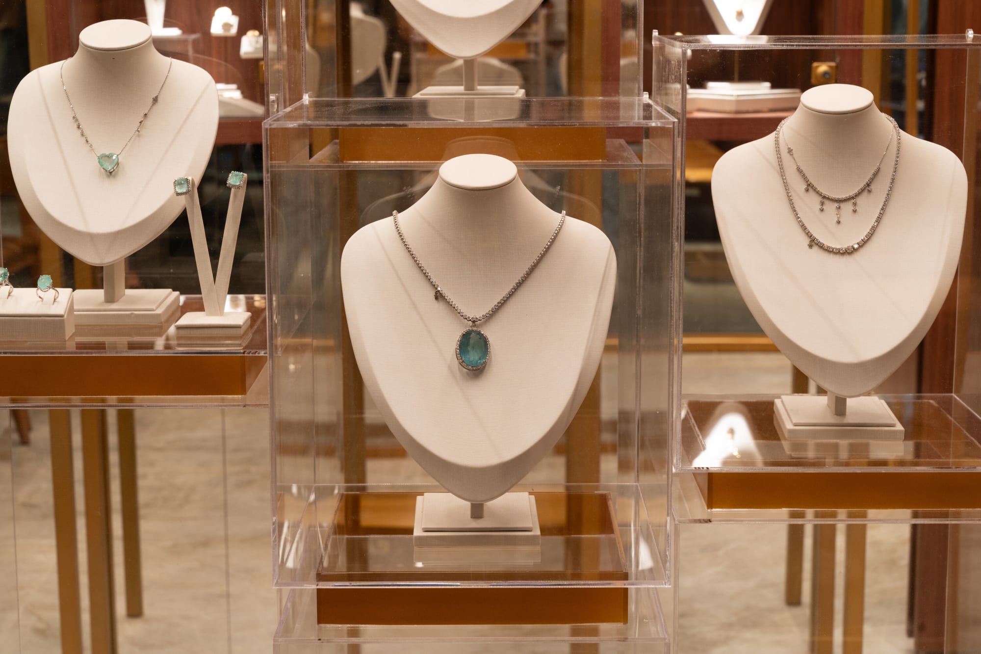 Victoria Pinheiro necklaces with green stones on white busts inside acrylic vitrines