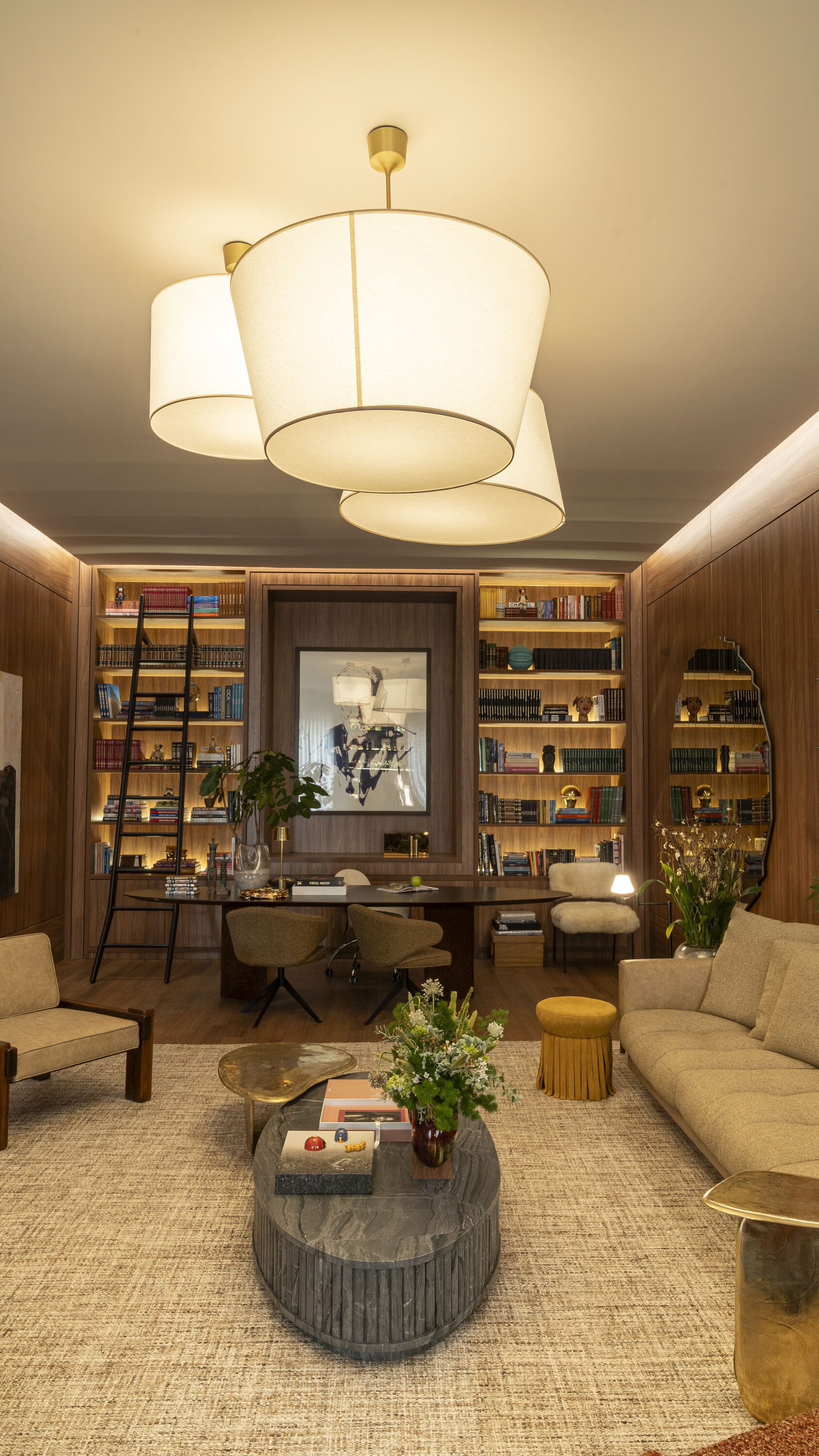 Living room with drum pendant lamps, lit bookshelves and a ribbed coffee table on a woven rug