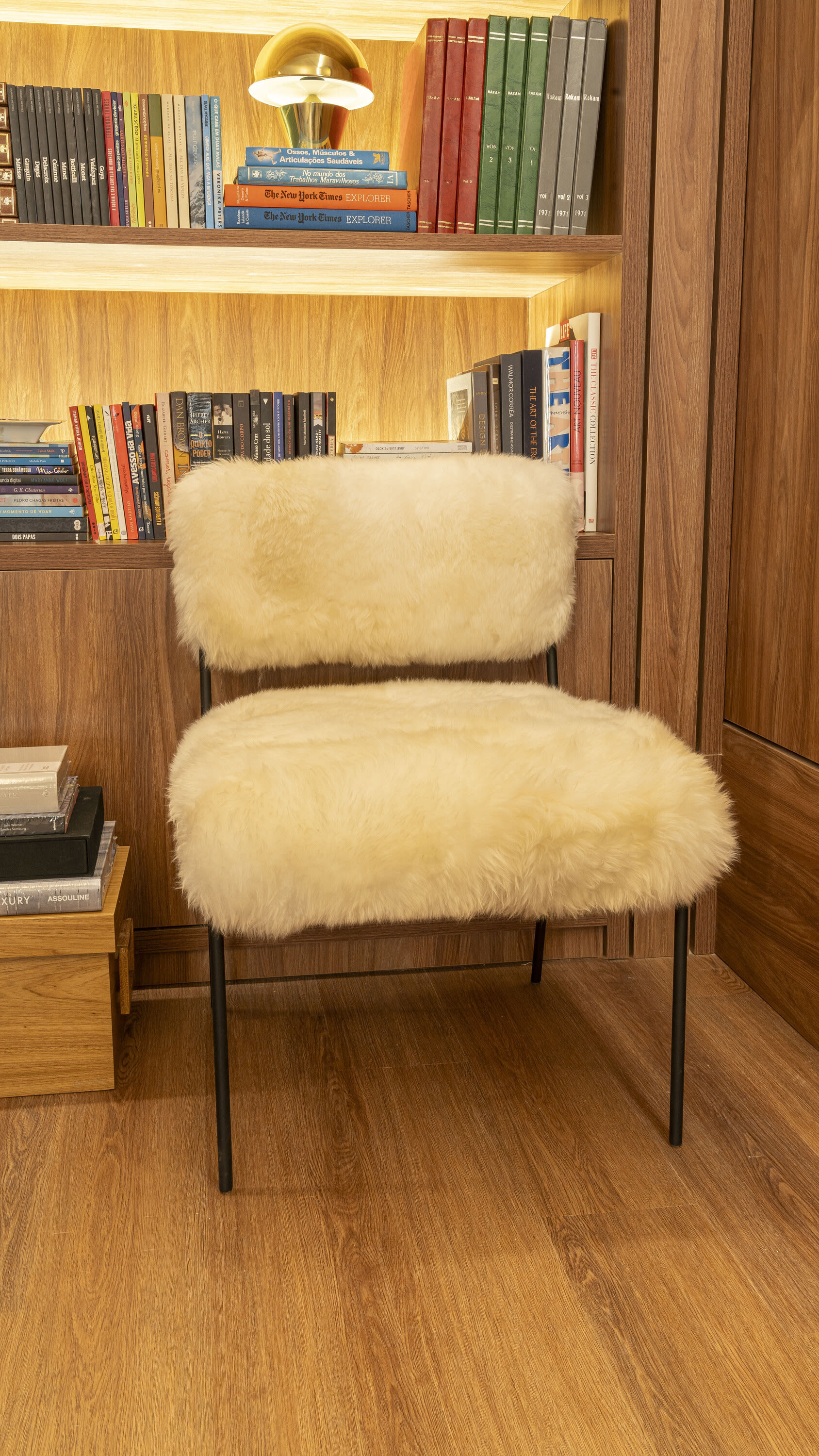 White sheepskin chair in front of a lit bookshelf on an oak floor