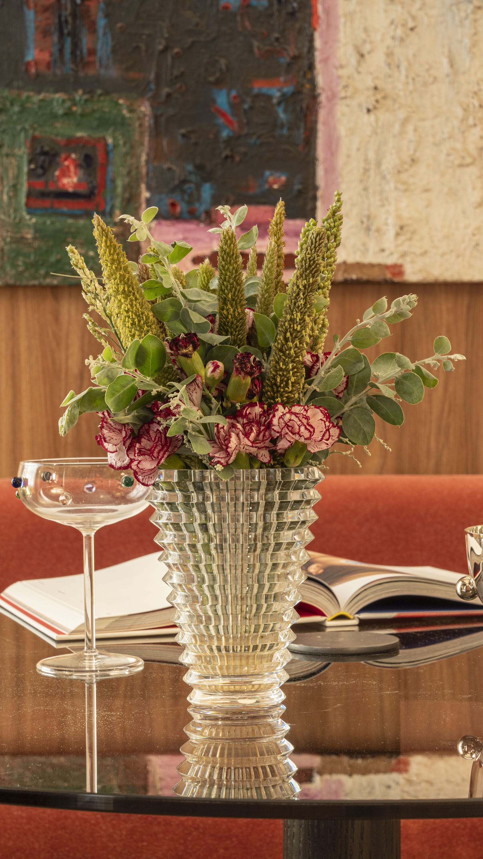 Cut crystal vase of dried flowers and a coupe glass on a dark table