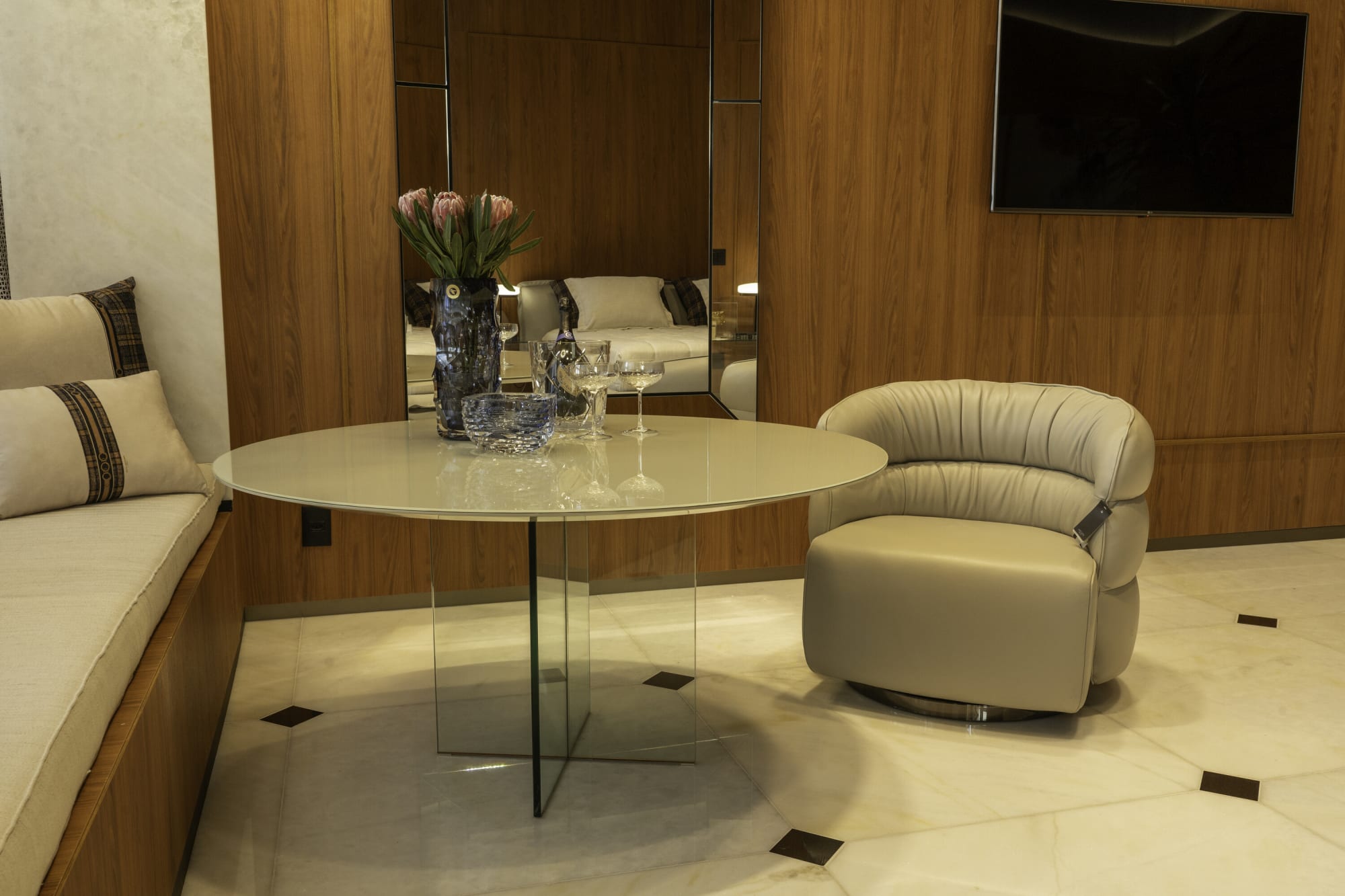 كرسي دوّار منحنٍ من Natuzzi بجانب طاولة مستديرة بقاعدة زجاجية ومقعد نافذة
