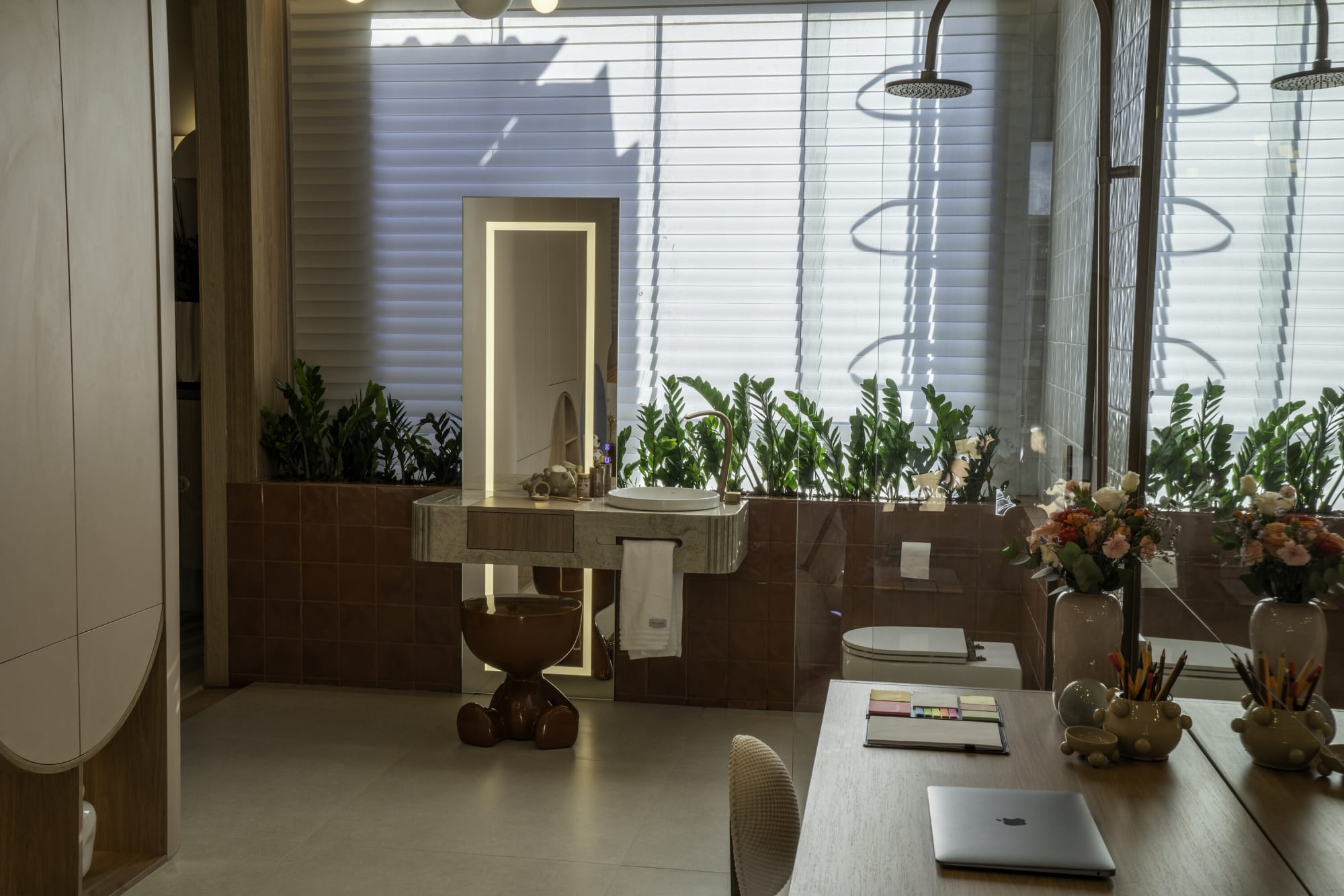 Study desk, lit mirror and planted bathroom counter seen through a kids' suite