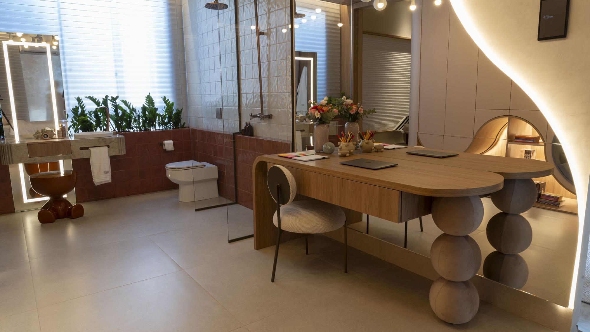 Oak desk on stacked sphere legs facing a backlit mirror and green planter