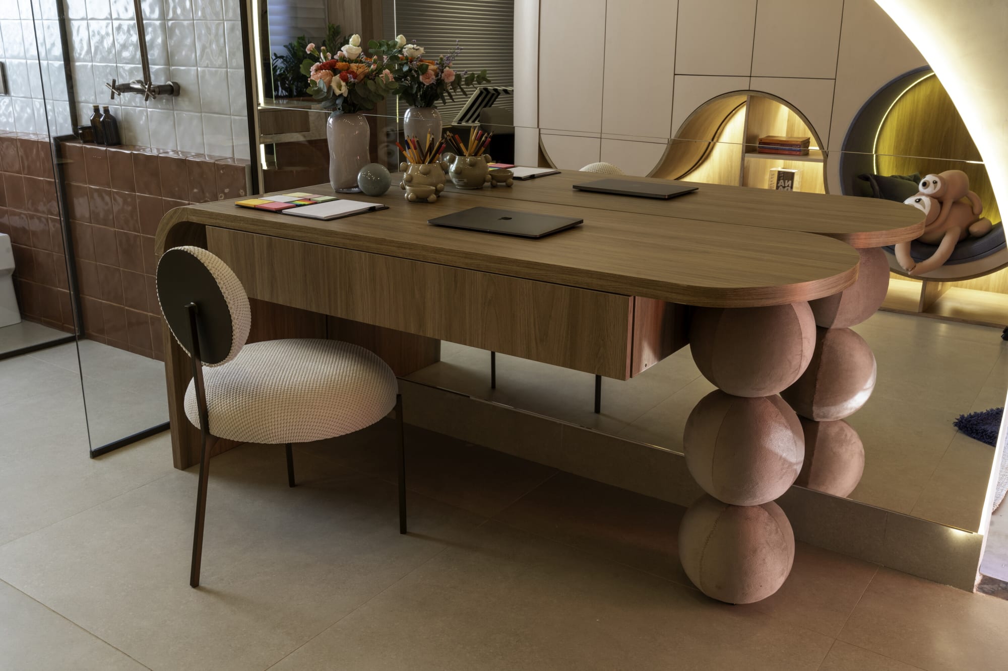 Wooden desk with ball legs and a bouclé chair beside a glowing arched niche