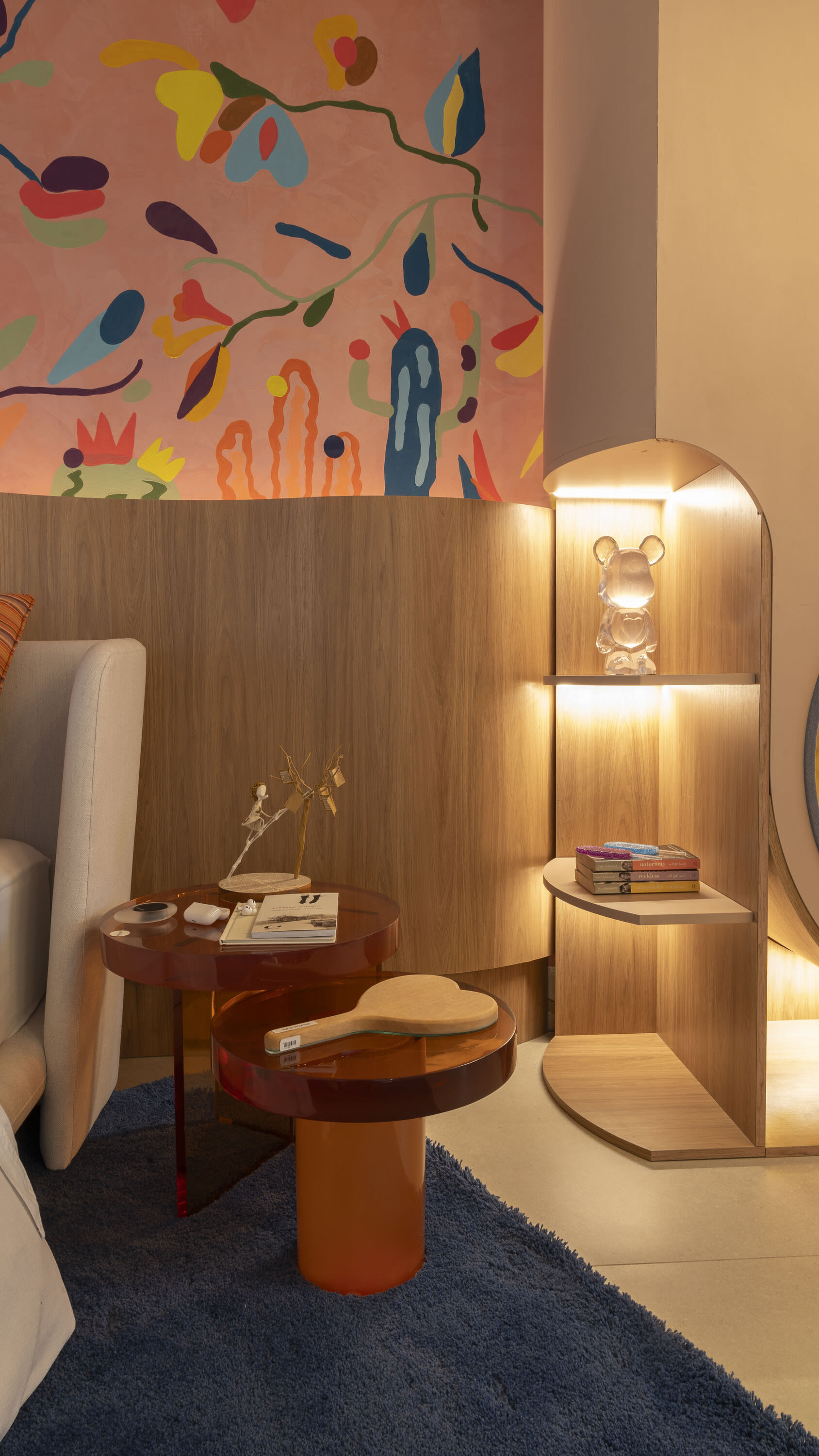 Rust side table and lit oak shelving beside an upholstered headboard and mural