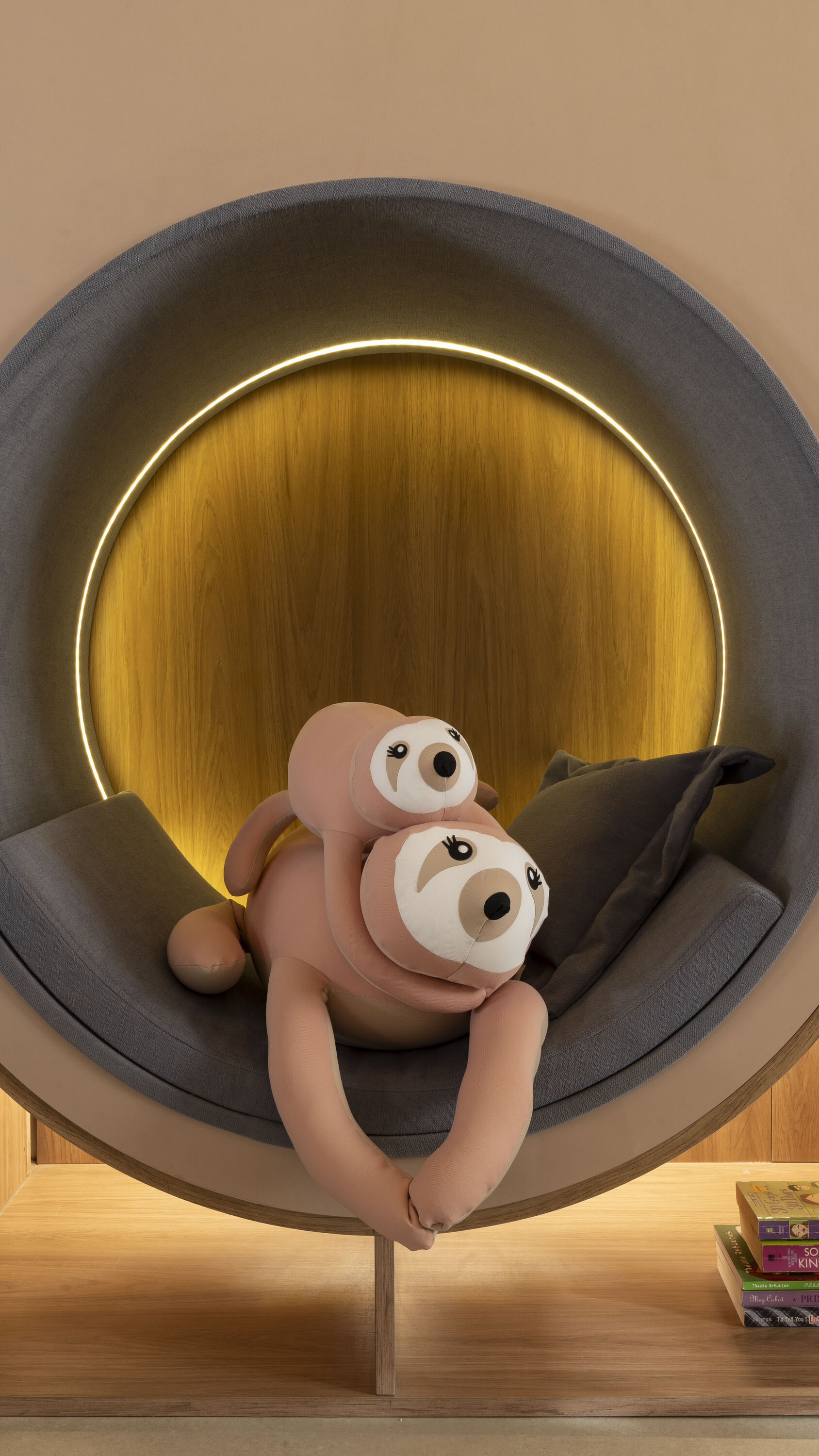 Plush sloth toy curled inside a round backlit oak reading nook